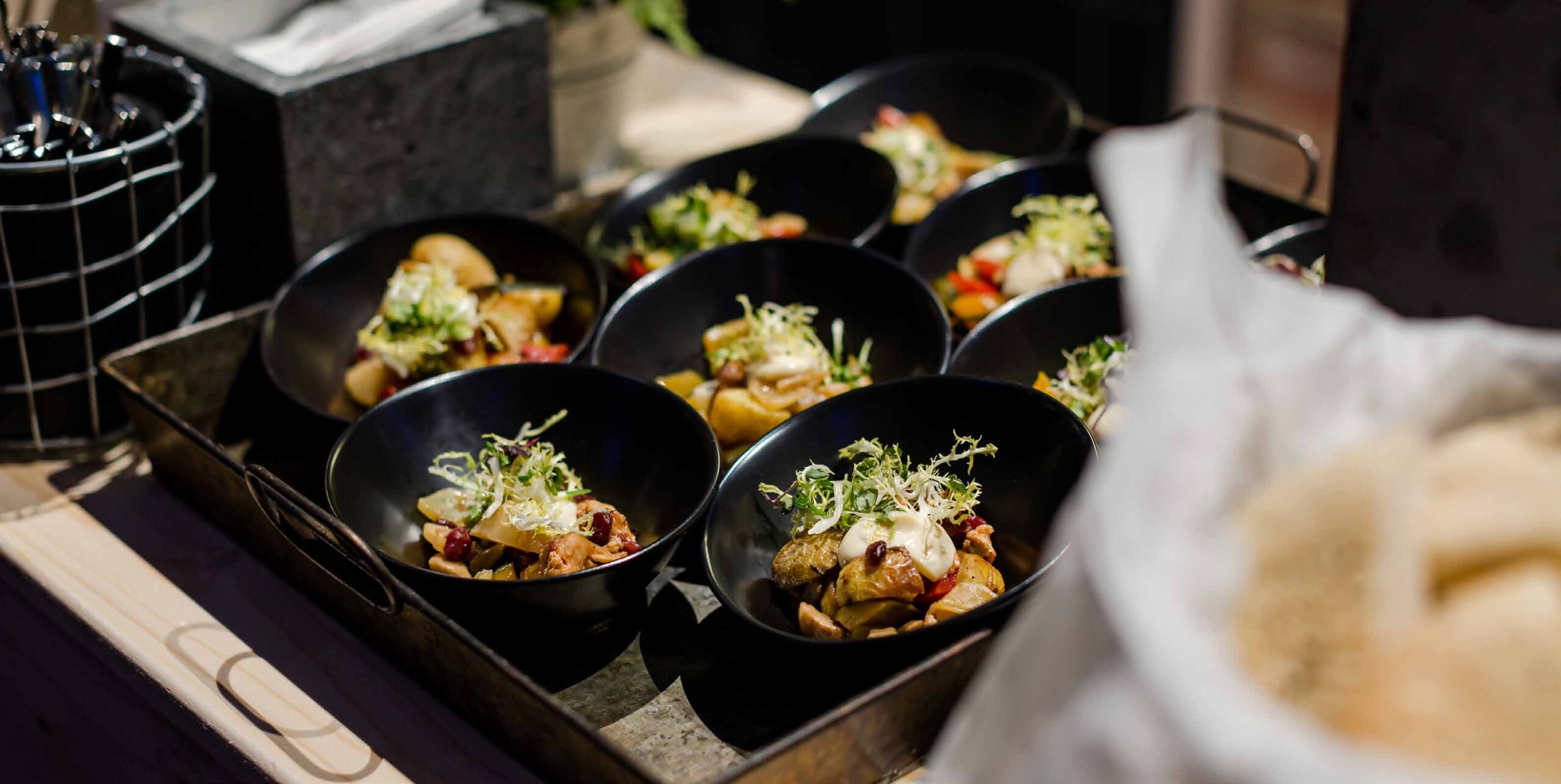 Schwarze Schalen, gefüllt mit Gourmetsalaten, sind auf einem Tablett angerichtet und bereit zum Servieren - perfekt für Eventcatering für besondere Anlässe.