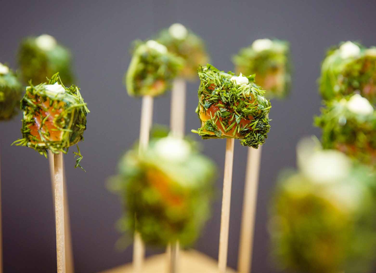Nahaufnahme von mit Kräutern ummantelten Vorspeisenwürfeln am Stiel, perfekt für Eventcatering für besondere Anlässe, mit leicht verschwommenem Hintergrund.