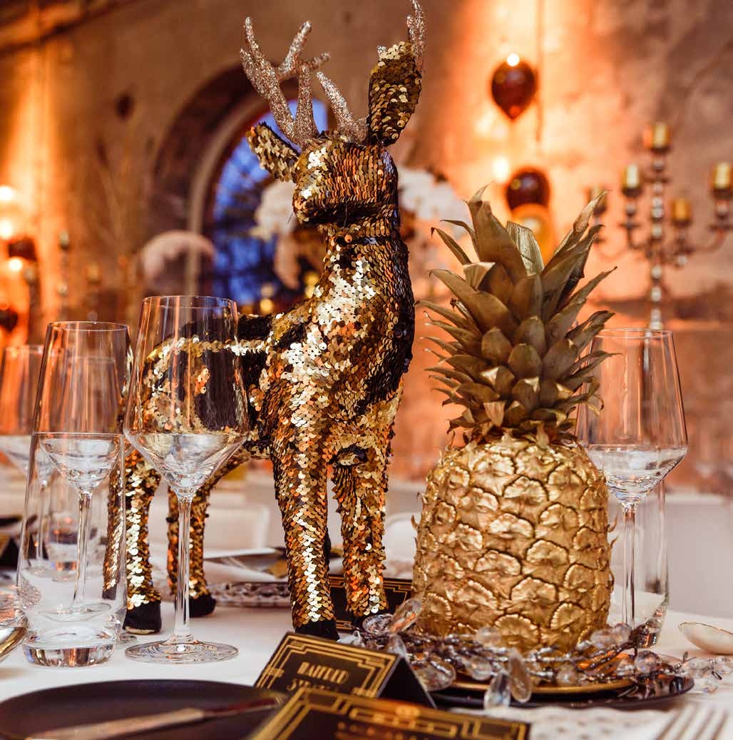 Ein festlich gedeckter Tisch mit einem goldenen Paillettenhirsch, einer goldbemalten Ananas, eleganten Gläsern - perfekt für Eventcatering für besondere Anlässe.