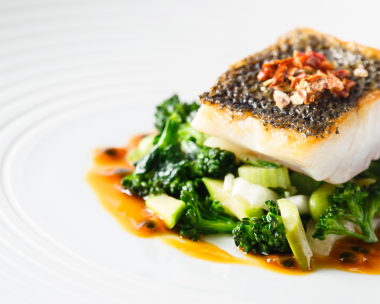 Gebratenes Fischfilet mit knuspriger Haut auf sautiertem Brokkoli und Grünzeug, garniert mit Sauce auf einem weißen Teller - perfekt für professionelles Catering für Events in Köln.