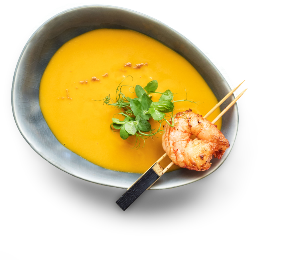 Schale mit cremiger Orangensuppe mit gegrillten Garnelenspießen und frischem Grün obendrauf.