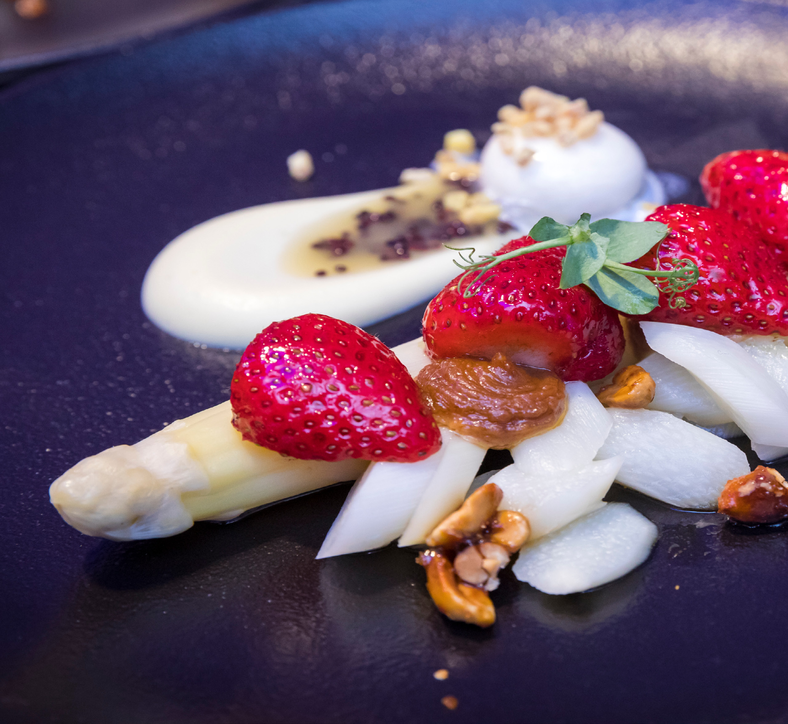 Weißer Spargel, Erdbeeren, Nüsse und Sauce elegant arrangiert auf einem dunklen Teller - perfekt für Eventcatering für besondere Anlässe.