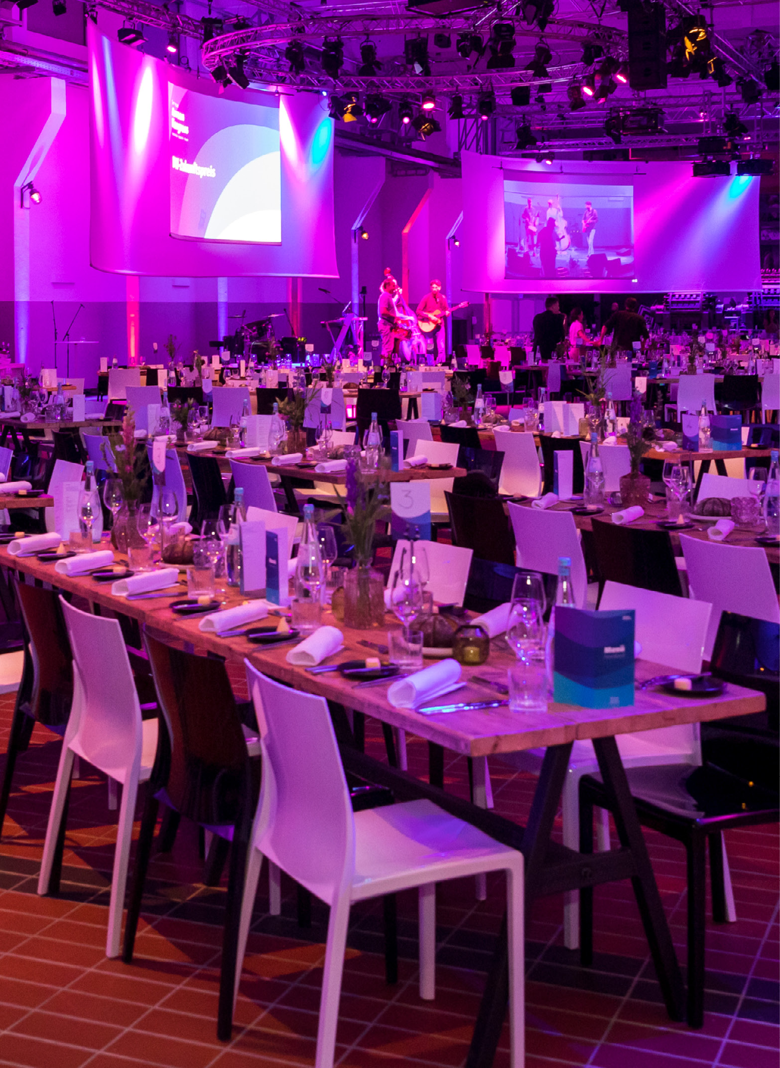 Ein Bankettsaal mit dekorierten Tischen, Bühne, violetter Beleuchtung und Musikern im Hintergrund - perfekt für Eventcatering für besondere Anlässe.