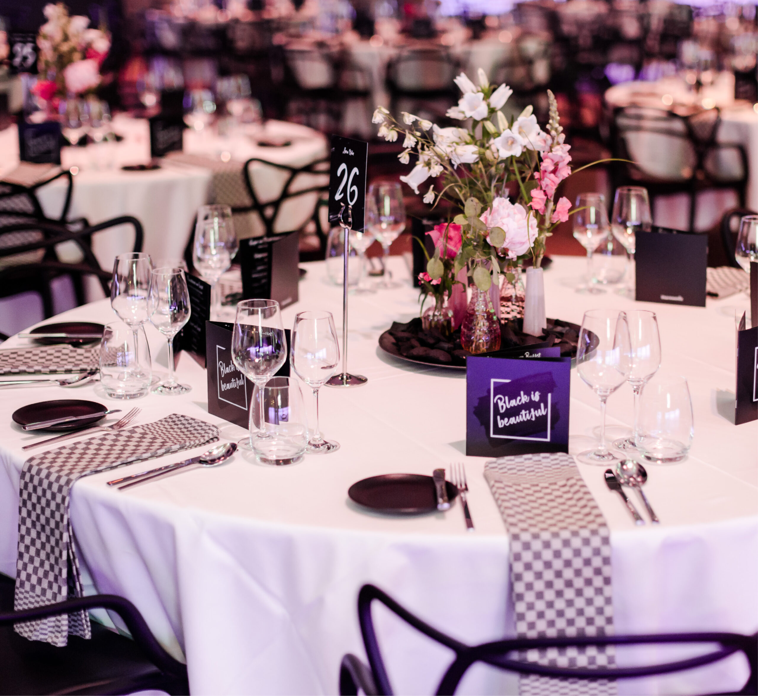 Eleganter runder Tisch für eine Veranstaltung, mit Blumen, Gläsern und einem "Black is beautiful"-Schild - perfekt für Eventcatering für besondere Anlässe.