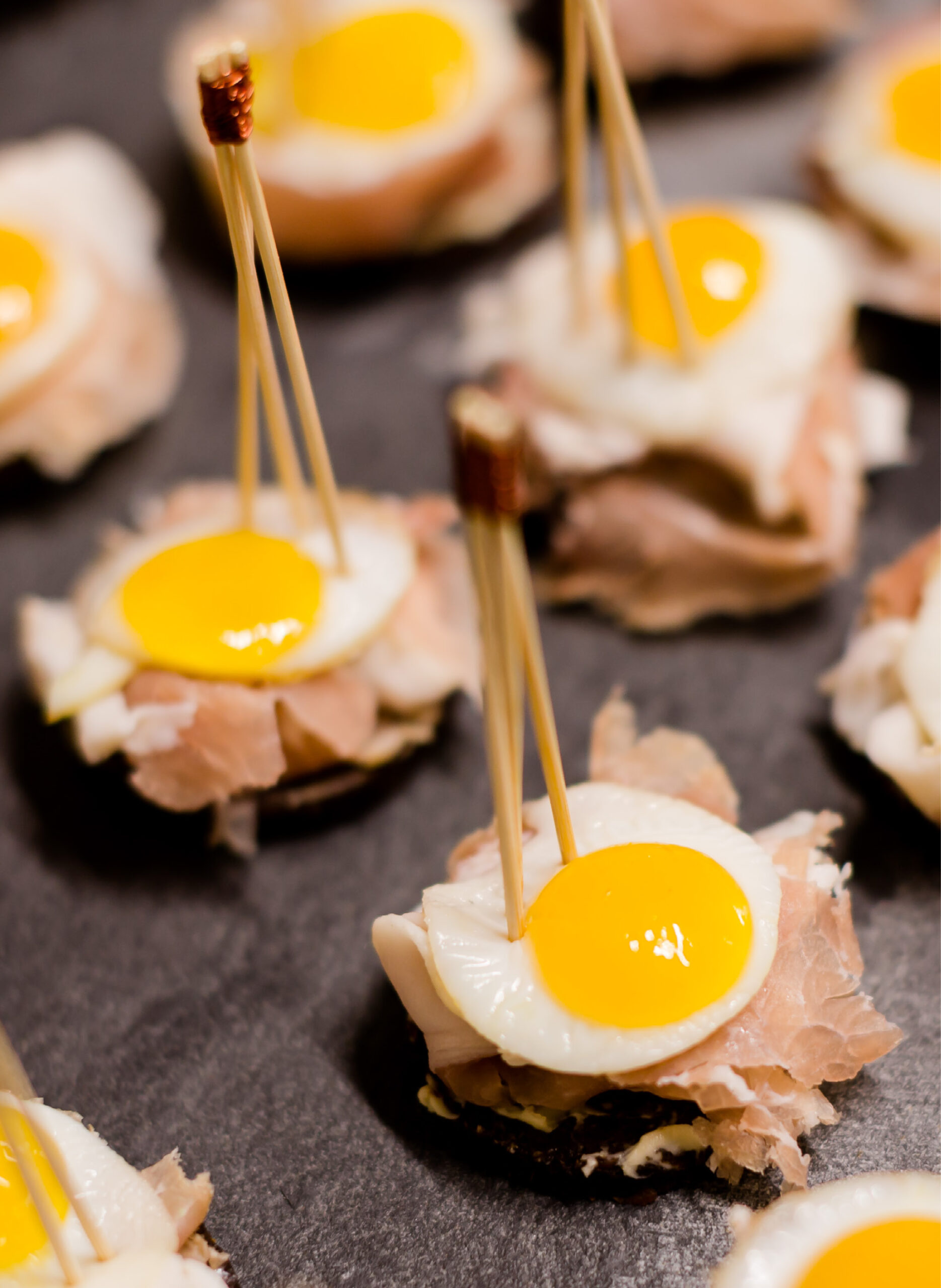 Mini-Wachteleier auf Prosciutto, serviert auf Brot mit Zahnstochern - ideal für Eventcatering für besondere Anlässe und sicher, um Ihre Gäste zu beeindrucken.