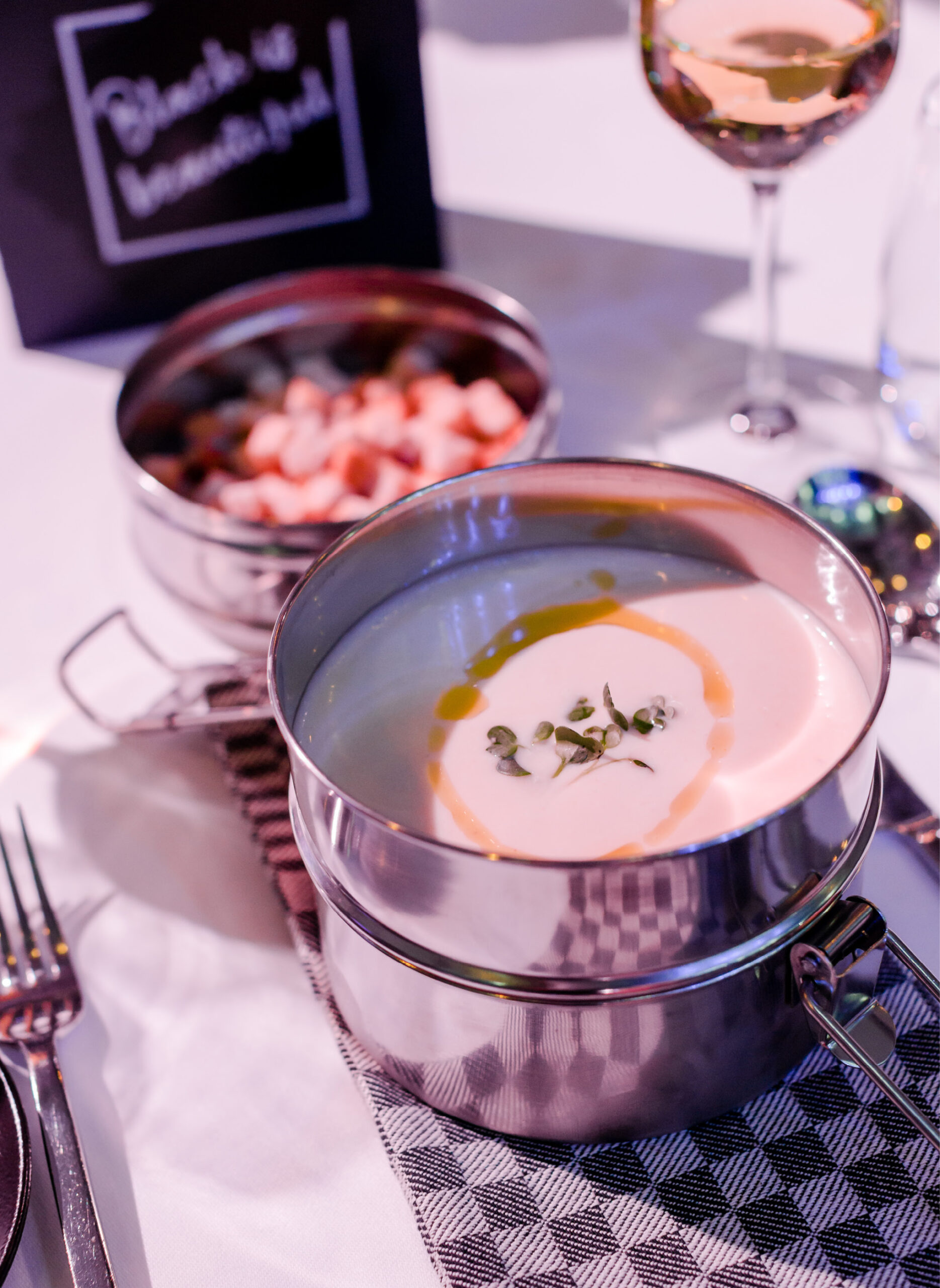 Eine Schale mit cremiger Suppe mit Kräutern und Öl, daneben ein Teller mit gewürfelten Speisen auf einer karierten Serviette - perfekt für Eventcatering für besondere Anlässe.