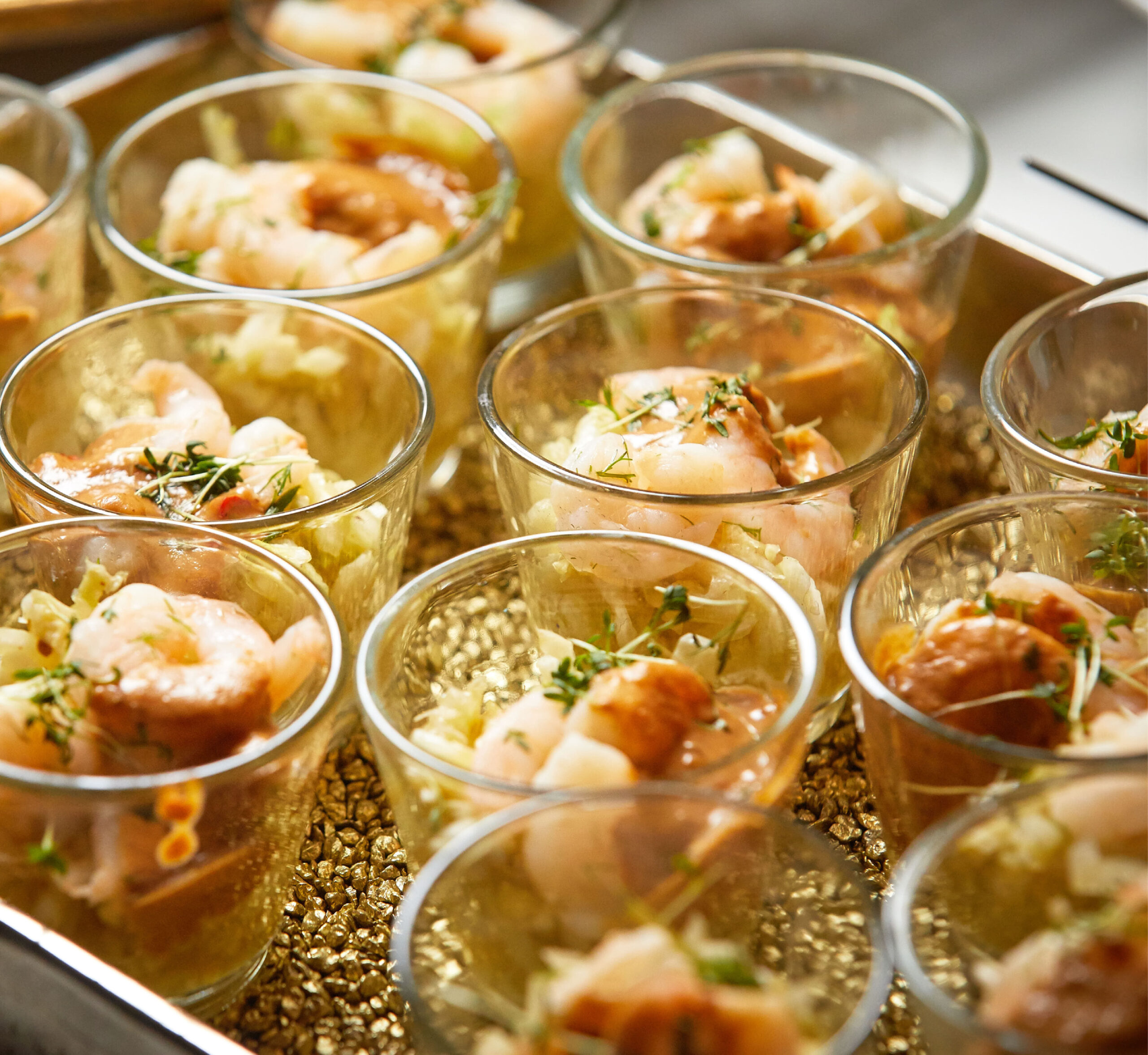 Kleine Glasschälchen, gefüllt mit Garnelen, Kräutern und einer leichten Sauce auf einem Tablett angerichtet - perfekt für Eventcatering für besondere Anlässe.