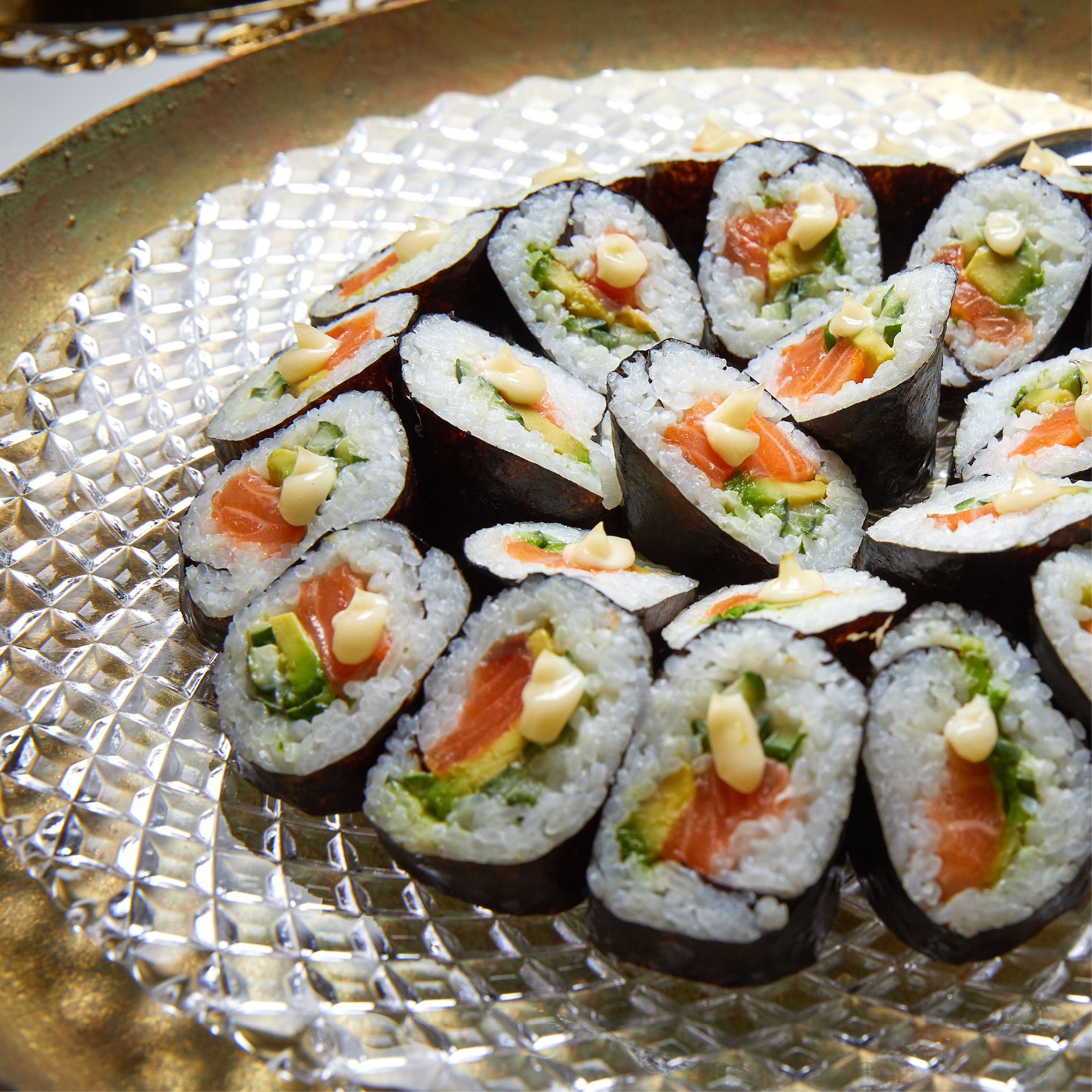 Sushi-Rollen mit Lachs, Avocado und Mayonnaise auf einer klar gemusterten Glasplatte - perfekt für Eventcatering für besondere Anlässe.