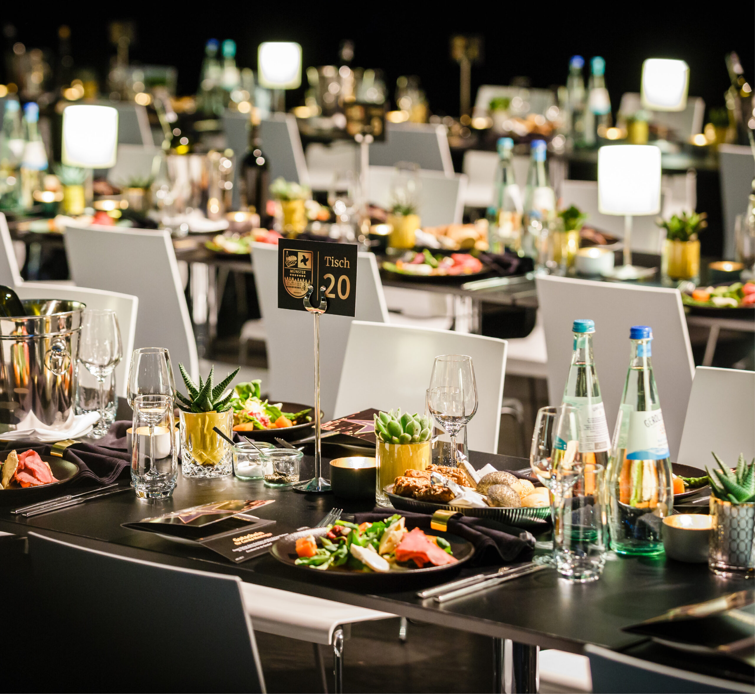 Elegant gedeckte Banketttische mit Tellern, Gläsern, Wasserflaschen und Tafelaufsätzen bei einem formellen Eventcatering für besondere Anlässe.