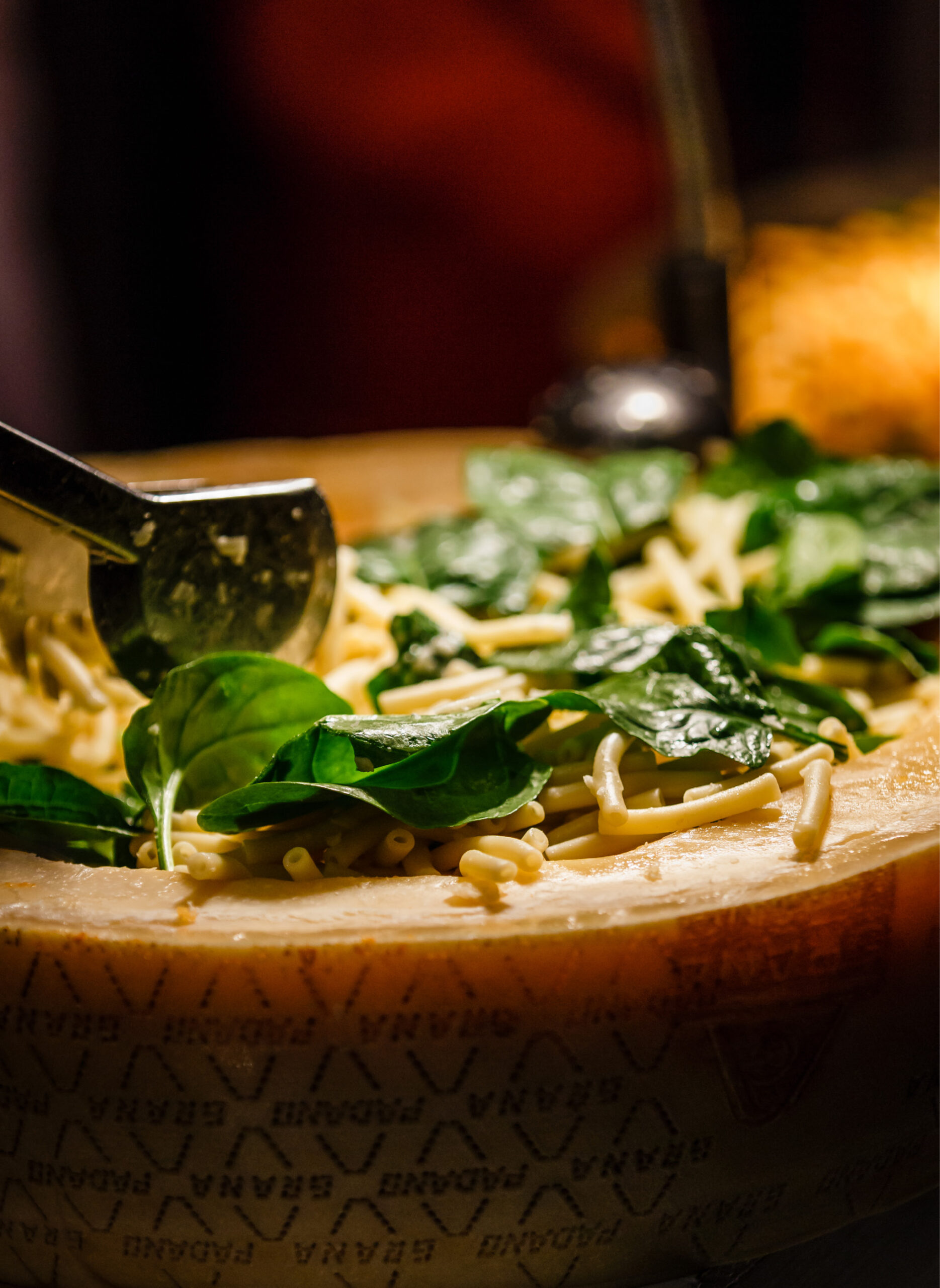 Frischer Spinat und Pasta werden aus einem großen Käselaib mit Zange serviert - perfektes Eventcatering für besondere Anlässe.