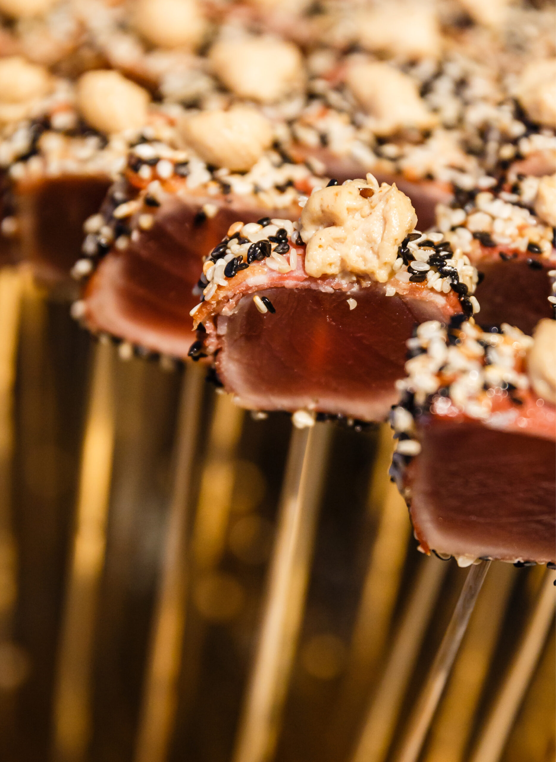 Nahaufnahme von gebratenen Thunfischspießen mit Sesamsamen und einem Klecks Sauce, perfekt für Eventcatering für besondere Anlässe.