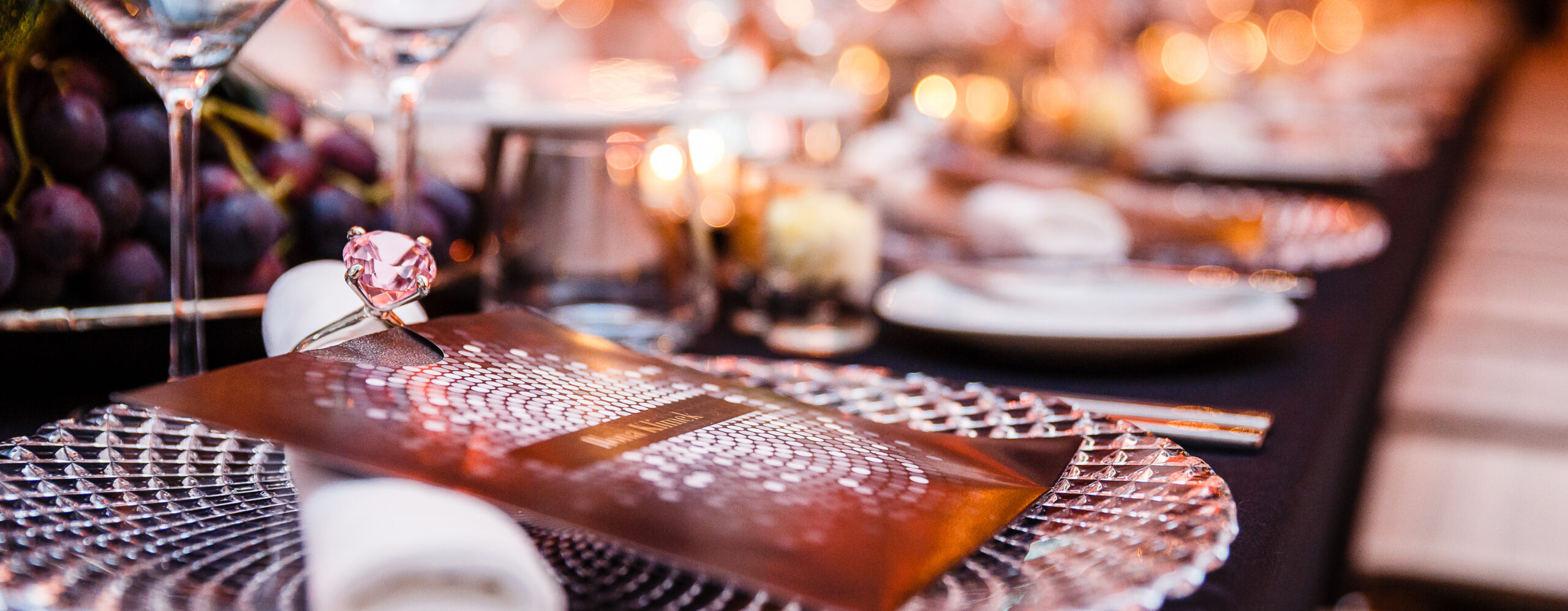 Elegant gedeckter Tisch mit Kristalltellern, einem rosa Edelstein-Serviettenring und einer funkelnden Menükarte.