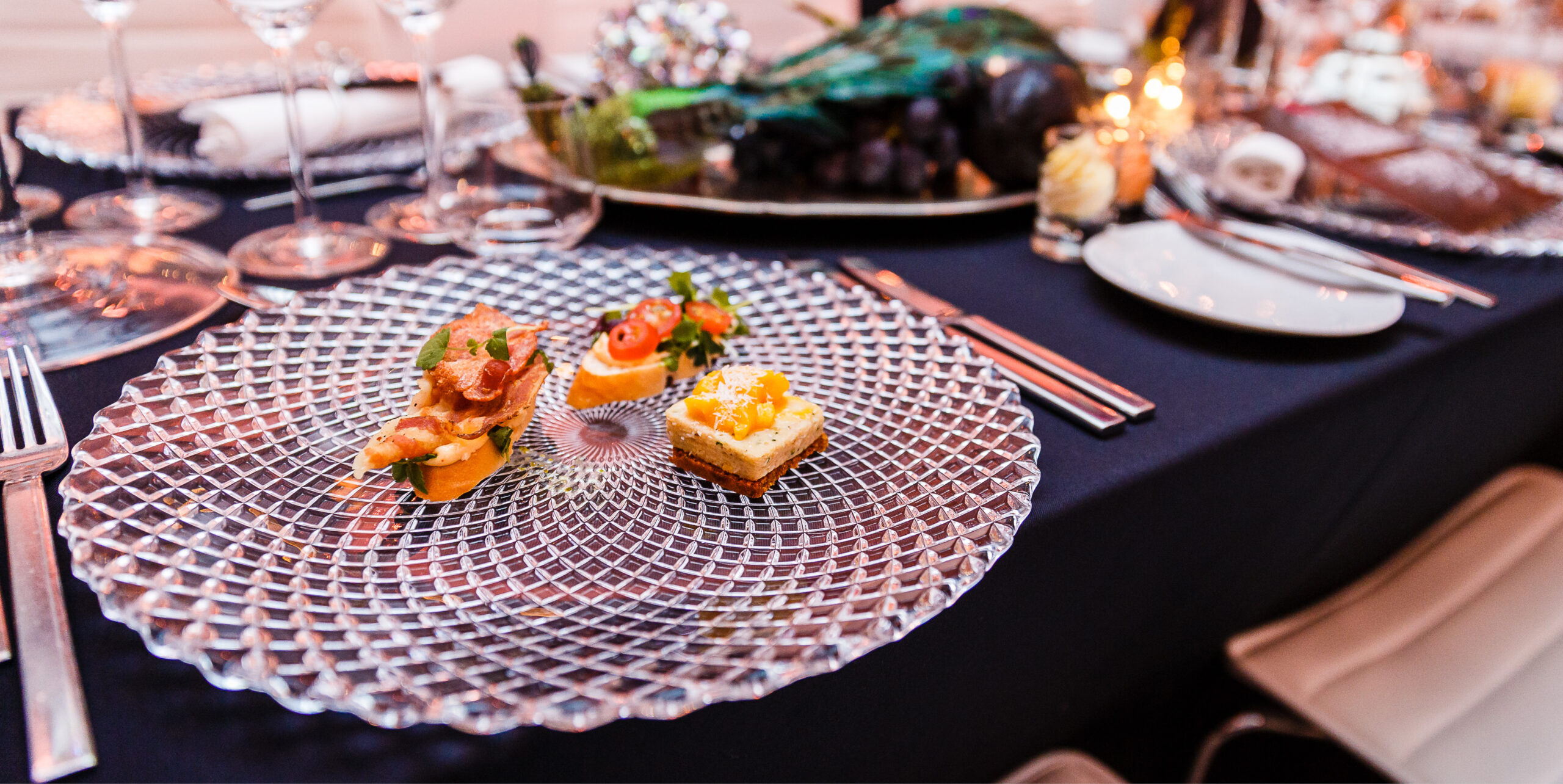 Elegantes Tischset mit einer Glasplatte mit zwei Gourmet-Häppchen auf einer dunklen Tischdecke, perfekt für Fine Dining Catering in Köln.