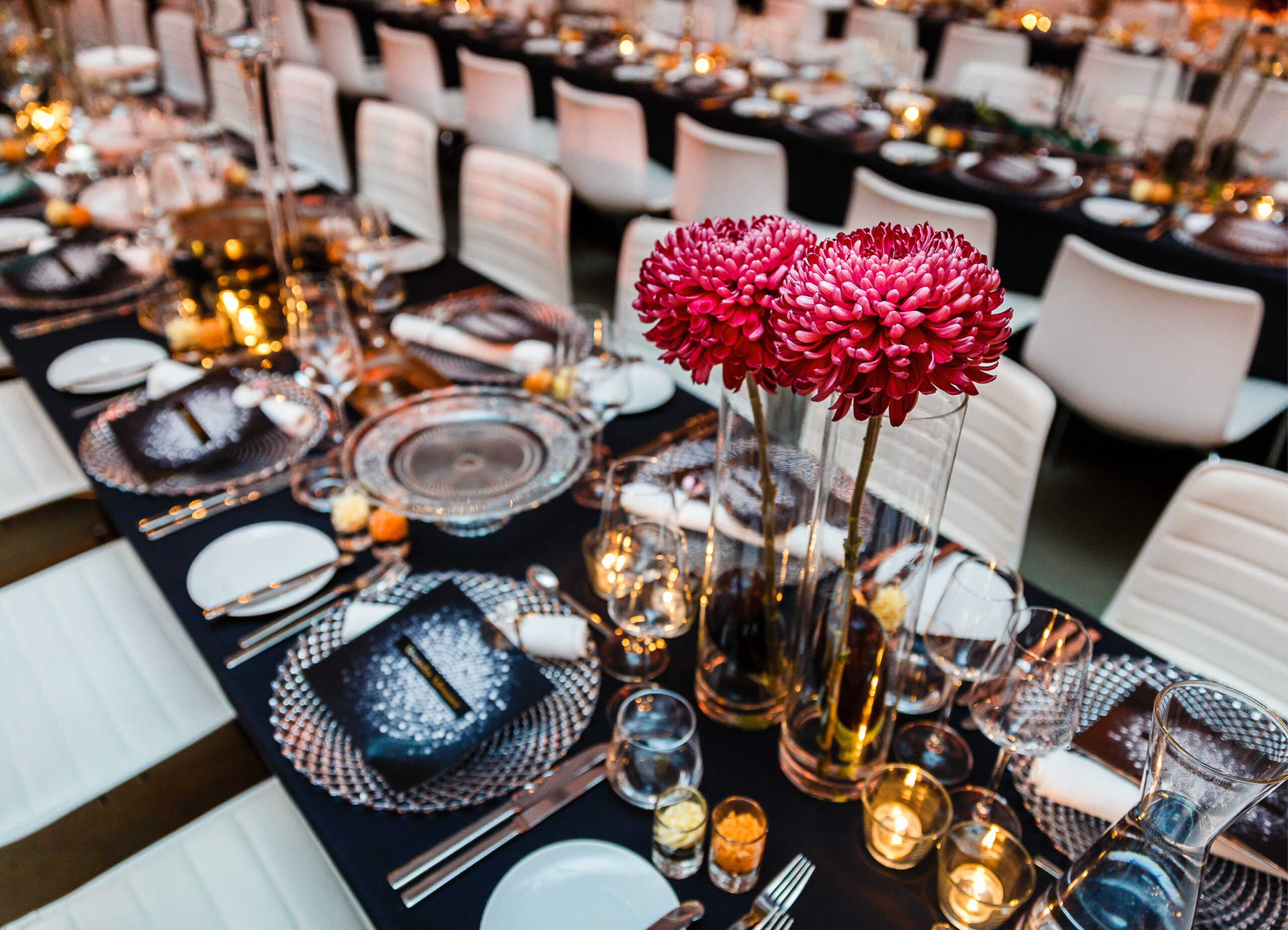 Elegante Tafel mit rosa Blumen, Kerzen und ordentlich arrangierten Tellern und Gläsern in einem formellen Rahmen - perfekt für Fine Dining Catering in Köln.