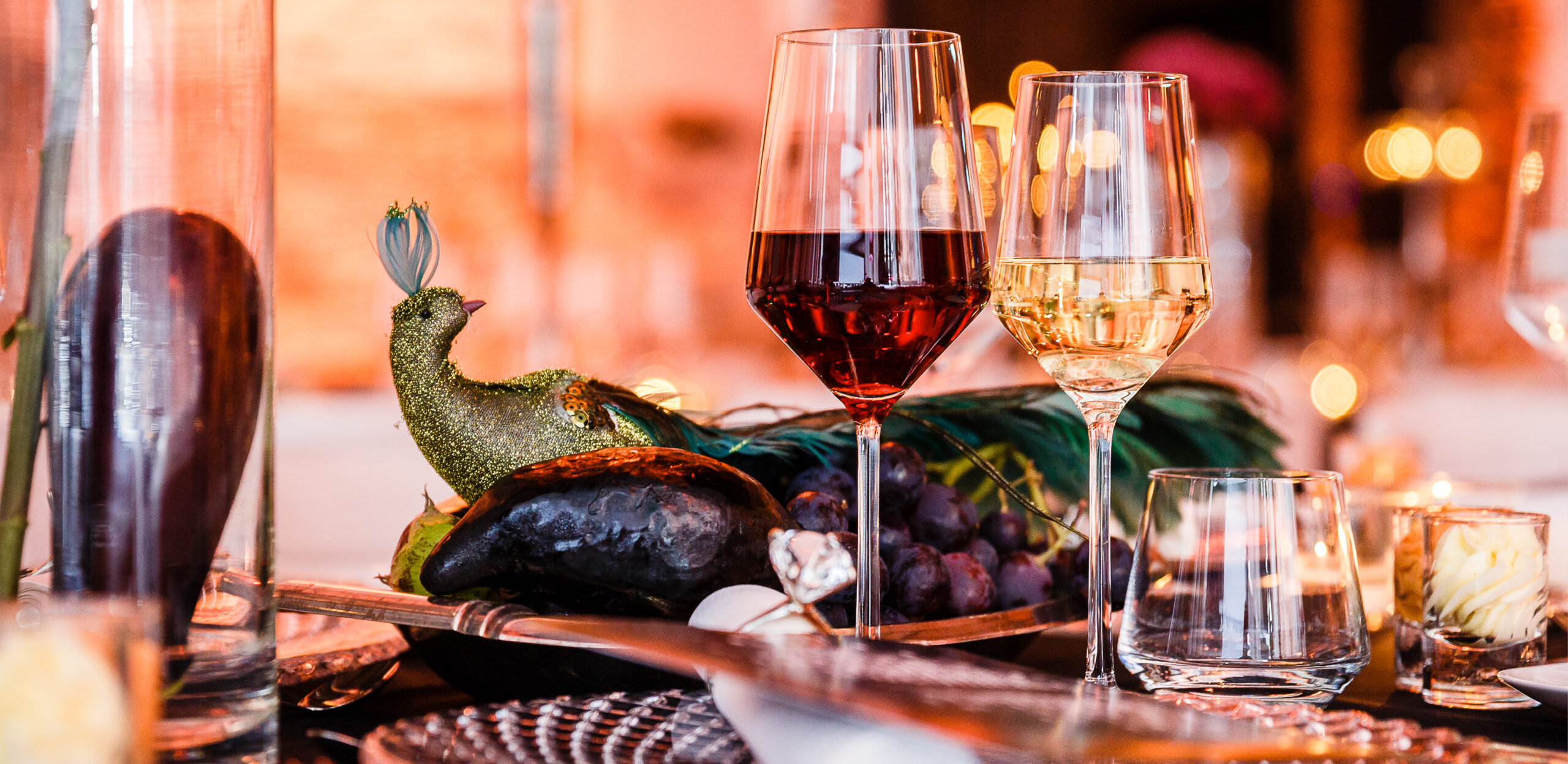Zwei Weingläser und ein Tafelaufsatz mit einem dekorativen Pfau, Weintrauben und eleganten Tischdecken - perfekt für Fine Dining Catering in Köln.