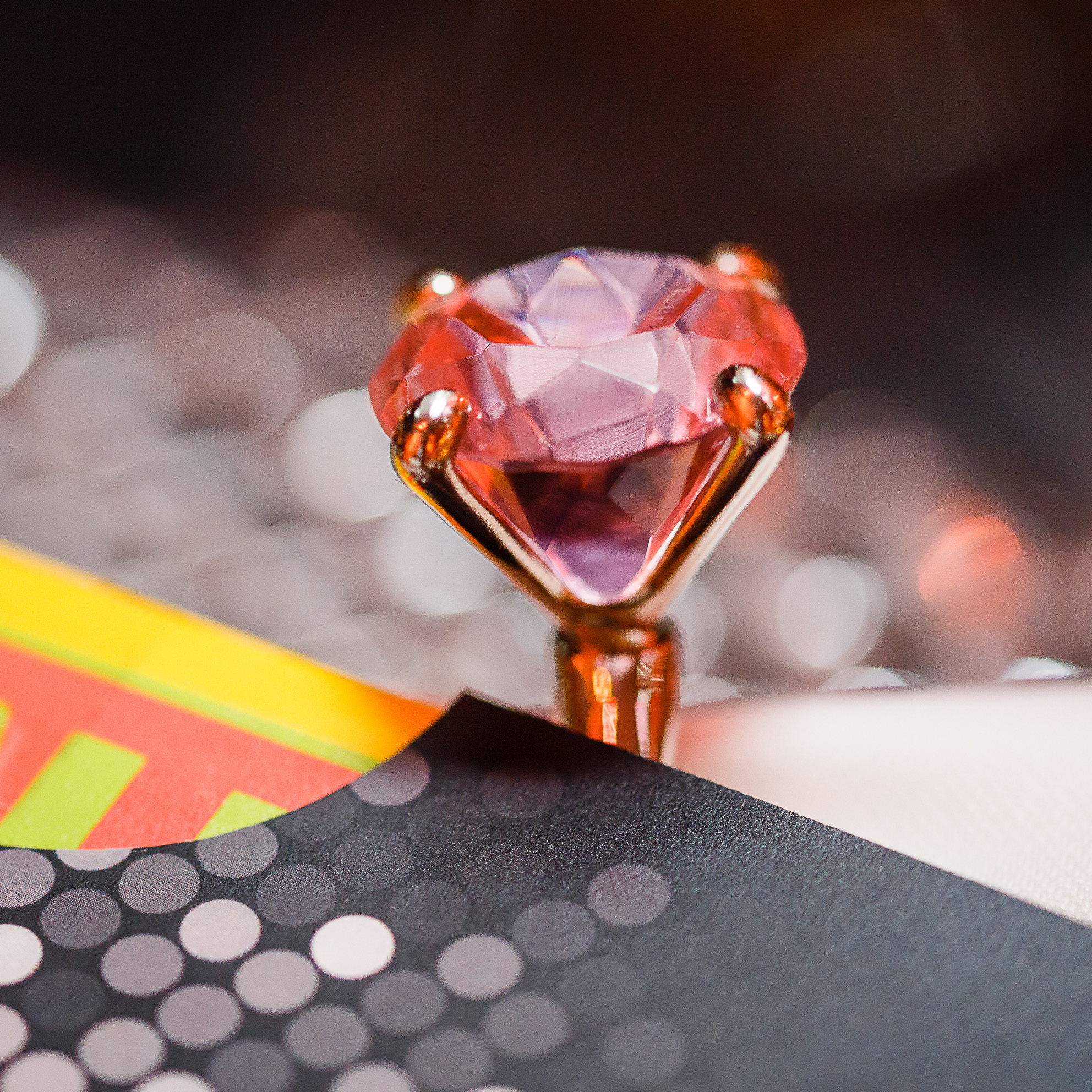 Eine Nahaufnahme eines Goldrings mit einem großen, facettierten rosa Edelstein auf einer bunten, gemusterten Oberfläche - eine elegante Note, die an das Fine Dining Catering in Köln erinnert.