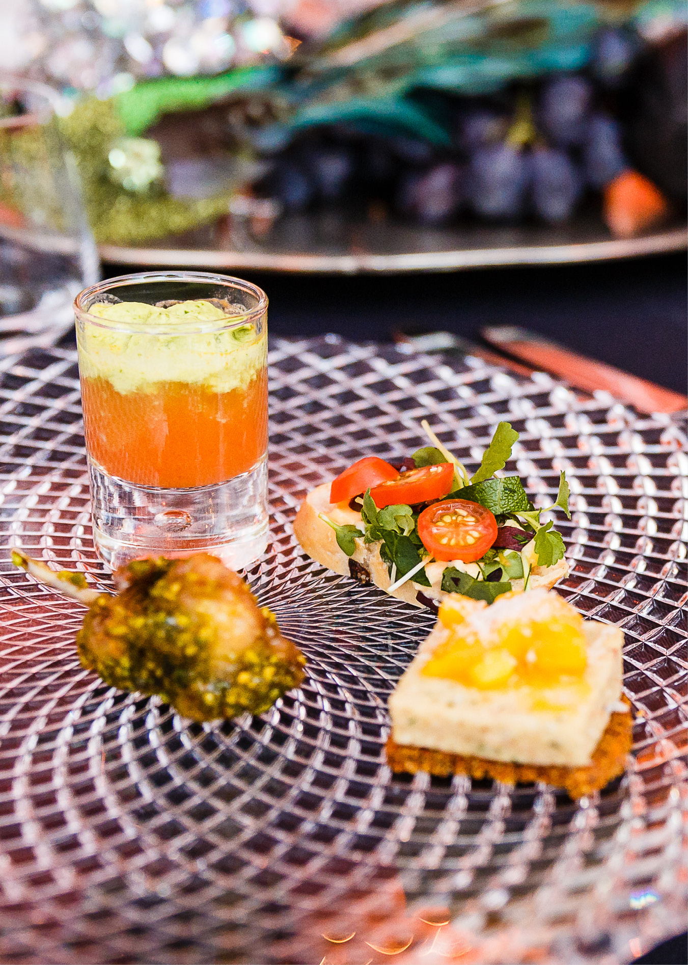 Ein Glas Schichtsuppe, eine gefüllte Tomate, ein Canapé und ein herzhafter Gemüsehappen auf einem Glasteller - perfekt präsentiert für Fine Dining Catering in Köln.