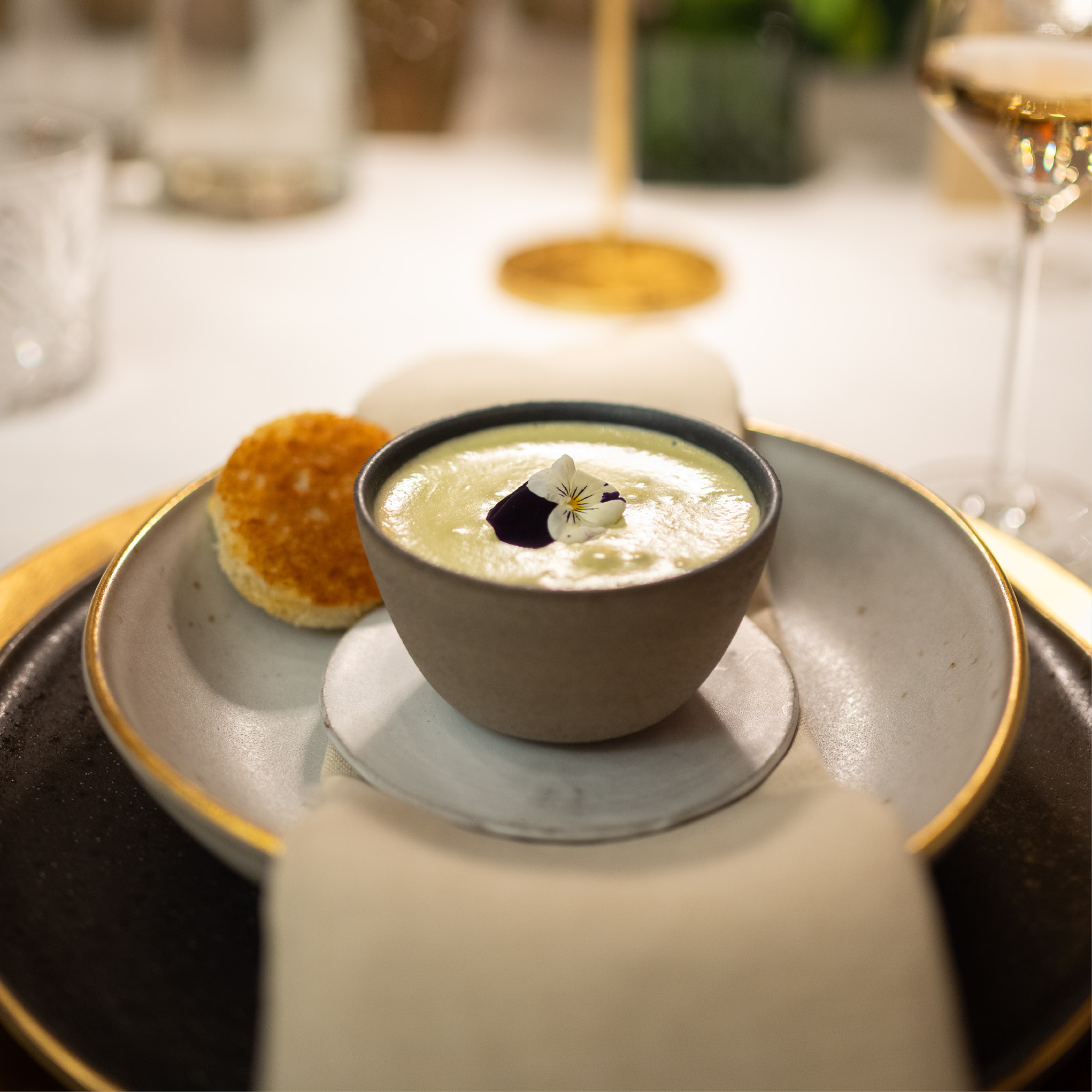 Eine Schale mit cremiger Suppe, garniert mit einer Blume, serviert mit einem runden Stück Brot auf einem weißen Teller - perfekt für Catering für Hochzeiten und Feiern.