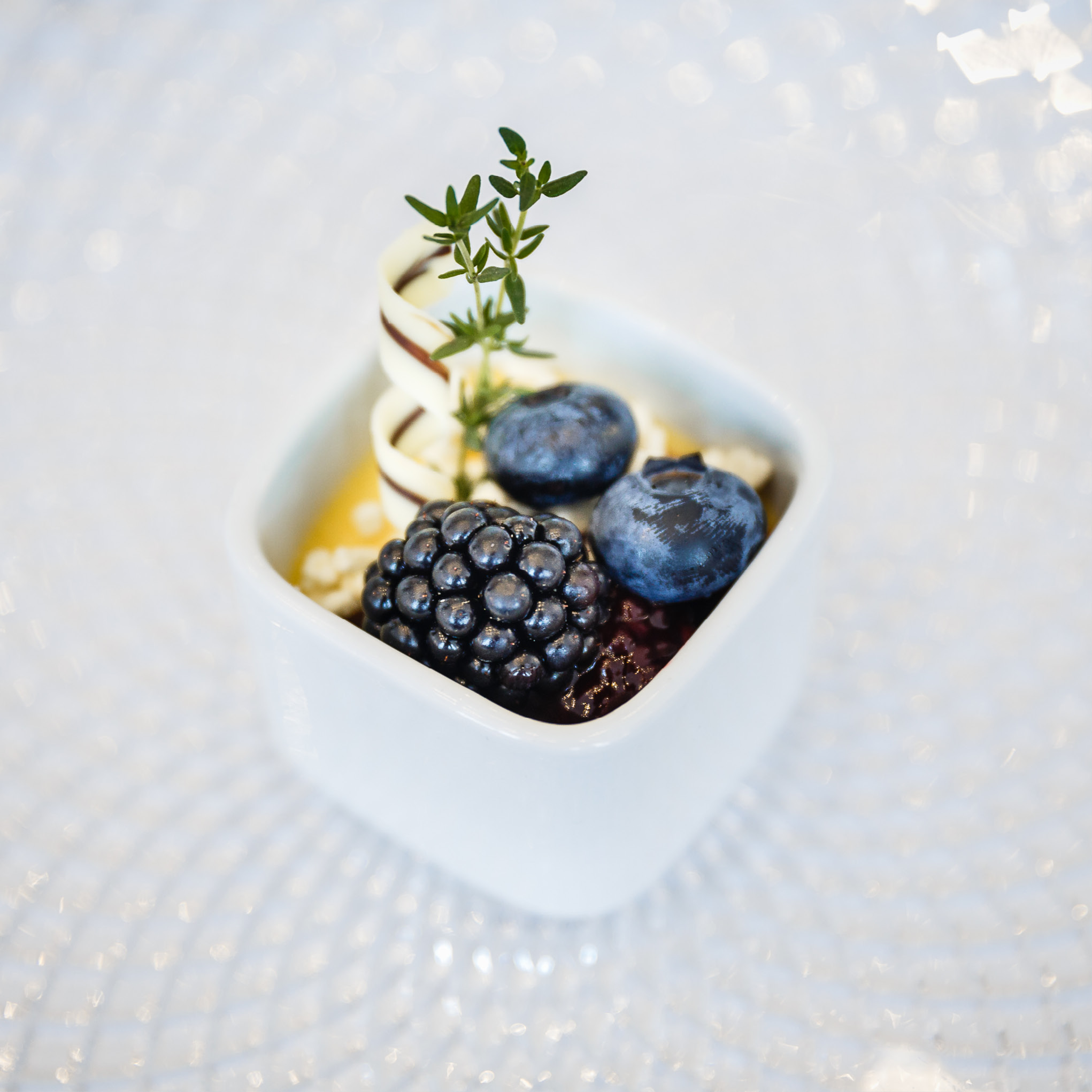 Kleiner Dessertbecher mit Brombeeren, Blaubeeren, weißen Schokoladenkringeln und einem Thymianzweig obenauf - ideal für Catering für Hochzeiten und Feiern.