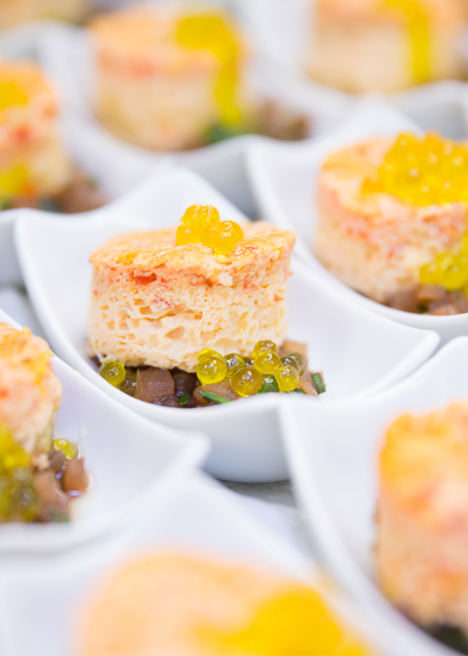 Nahaufnahme von Gourmet-Häppchen mit Mousse, gelber Garnitur und Gemüsewürfeln in weißen Servierschalen - ideal für Catering für Hochzeiten und Feiern.