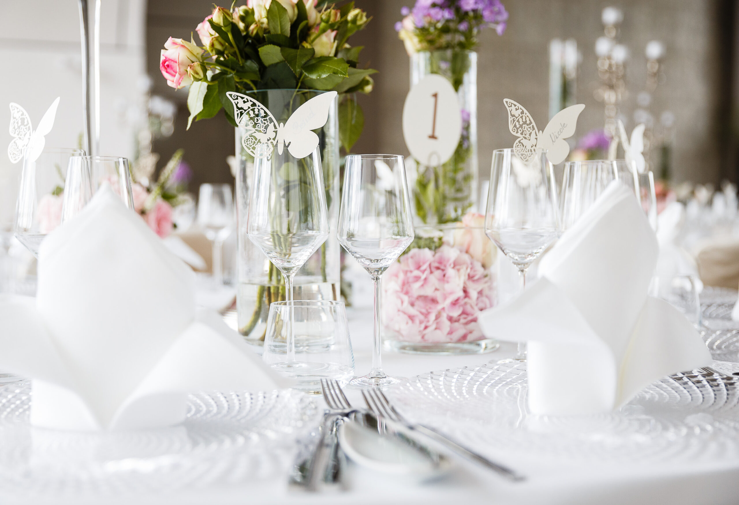 Eleganter Hochzeitstisch mit Blumen, Weingläsern, Schmetterlingsdekoration und gefalteten weißen Servietten - perfekt für Catering für Hochzeiten und Feiern.