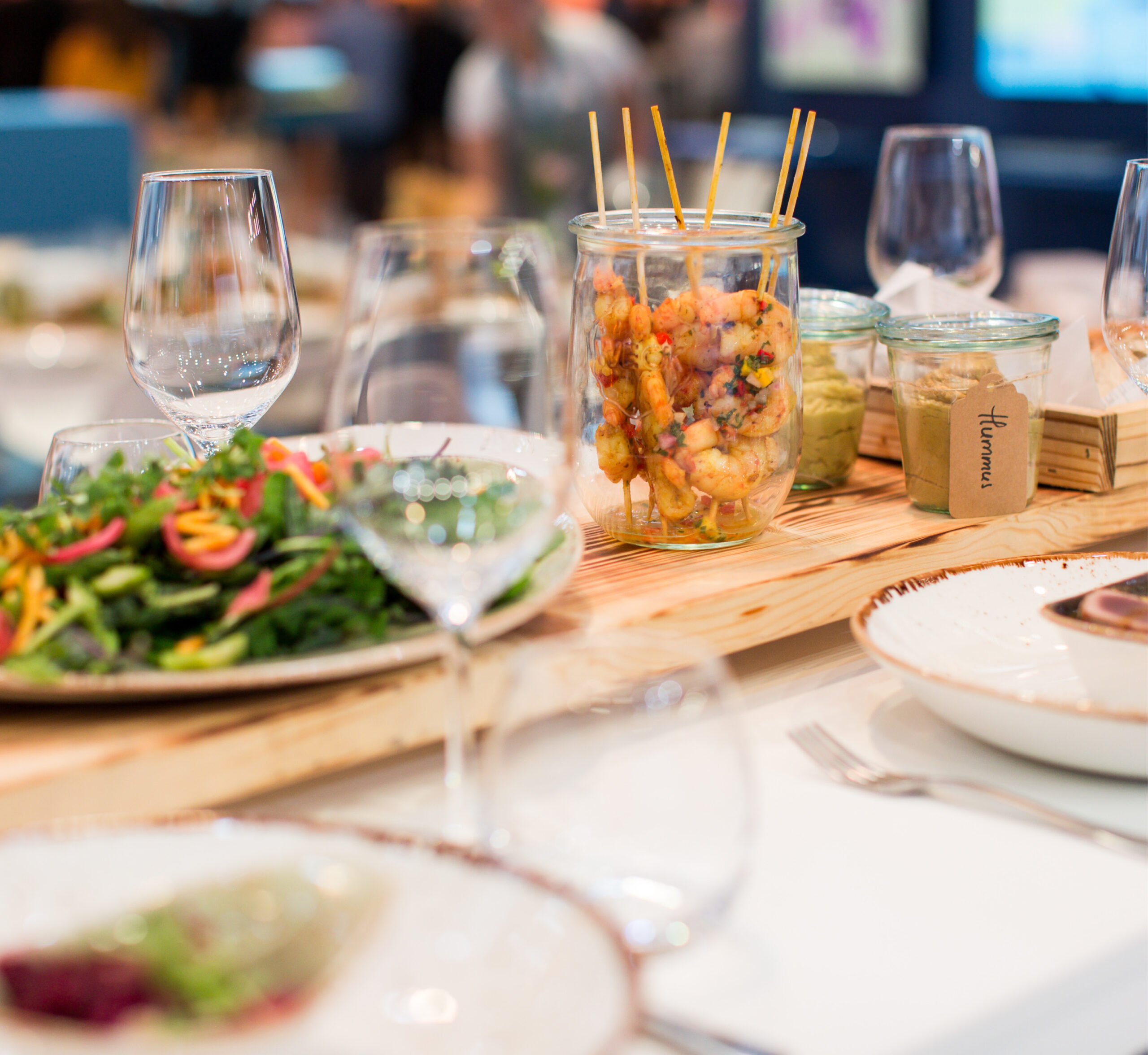 Der Tisch für das Messecatering für Veranstaltungen ist mit Salat, Vorspeisen in Gläsern, leeren Tellern und Weingläsern gedeckt - alles bereit für ein köstliches Essen.