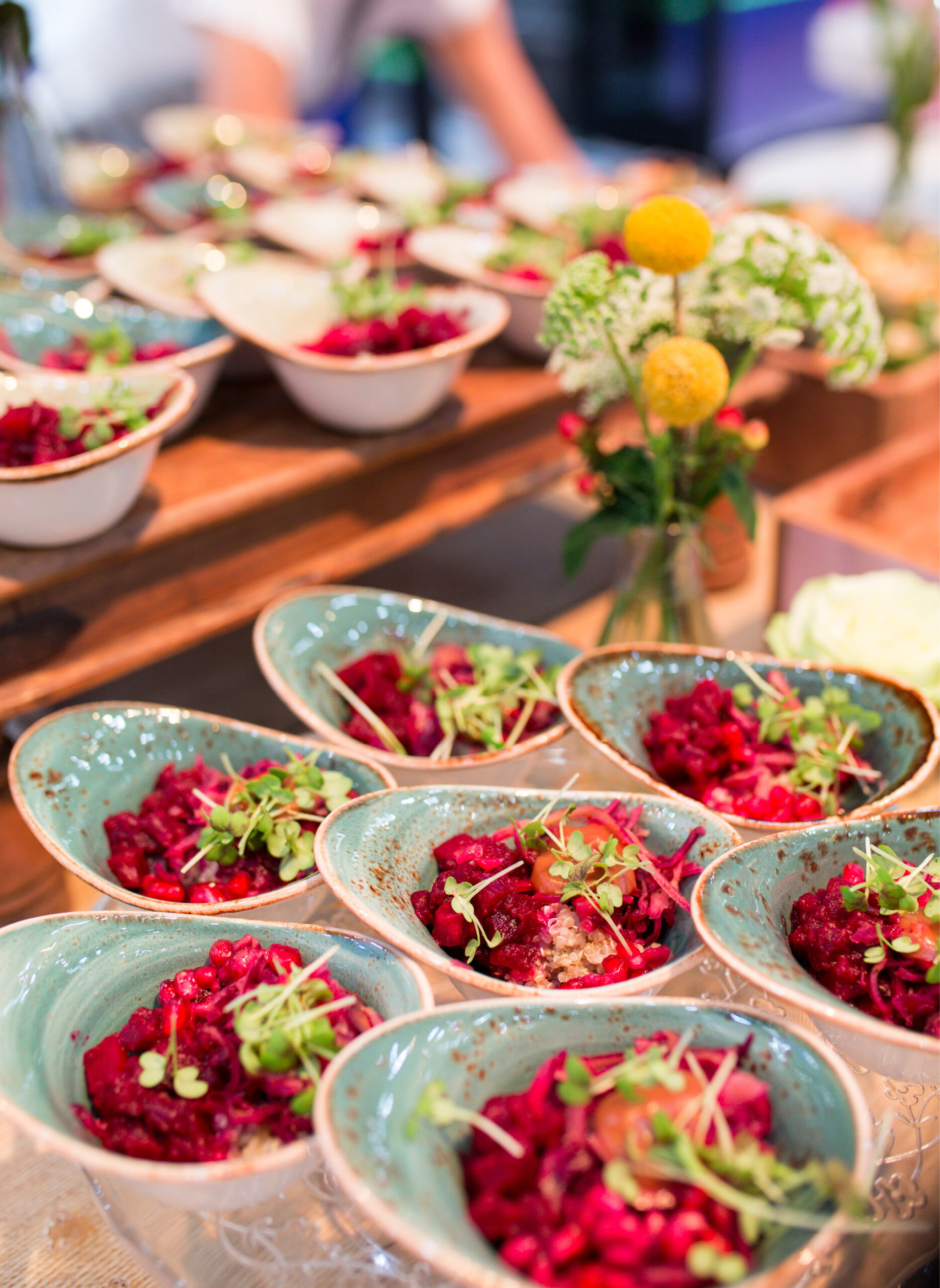 Kleine Schälchen mit lebhaftem Rübensalat und Mikrogrün, perfekt für das Messecatering für Veranstaltungen, auf einem Tisch mit dekorativen Blumen.