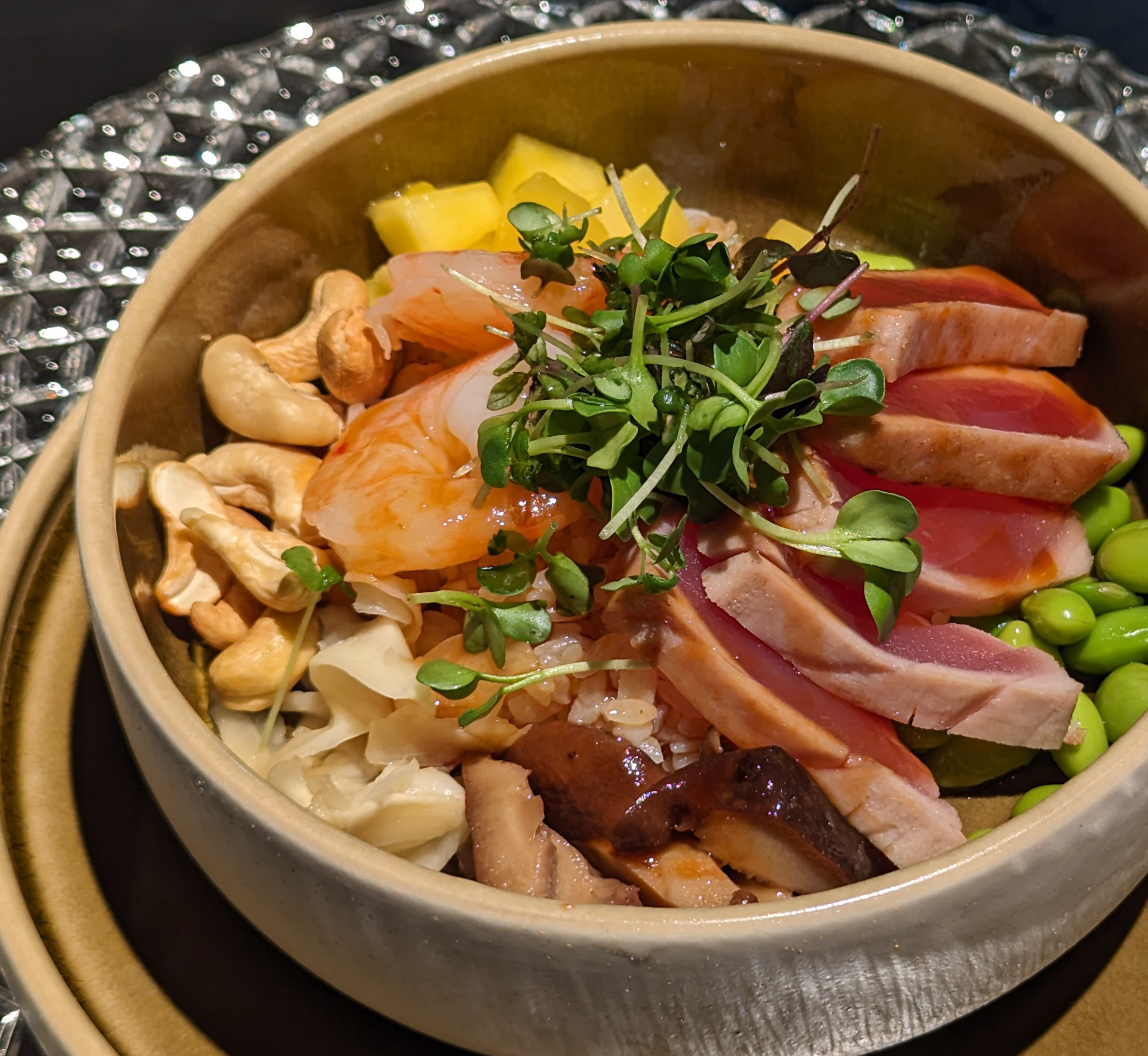 Eine Schüssel Poke mit geschnittenem Fisch, Mikrogrün, Cashews, Mango, Edamame und eingelegtem Ingwer.