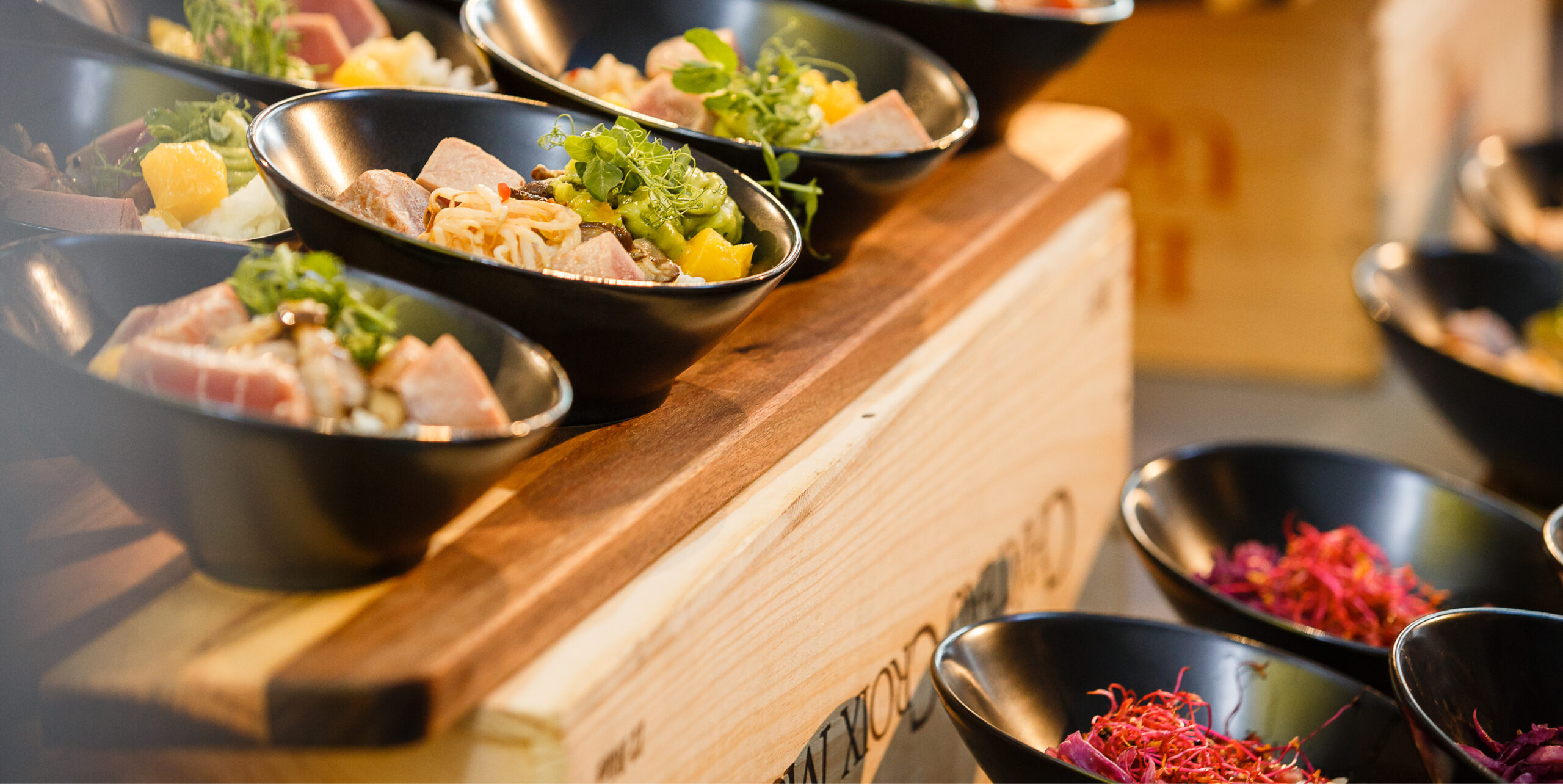 Auf einem hölzernen Servierbrett sind mehrere schwarze Schalen mit bunten, frischen Lebensmitteln angerichtet - ideal für das Catering für Tagungen und Konferenzen.