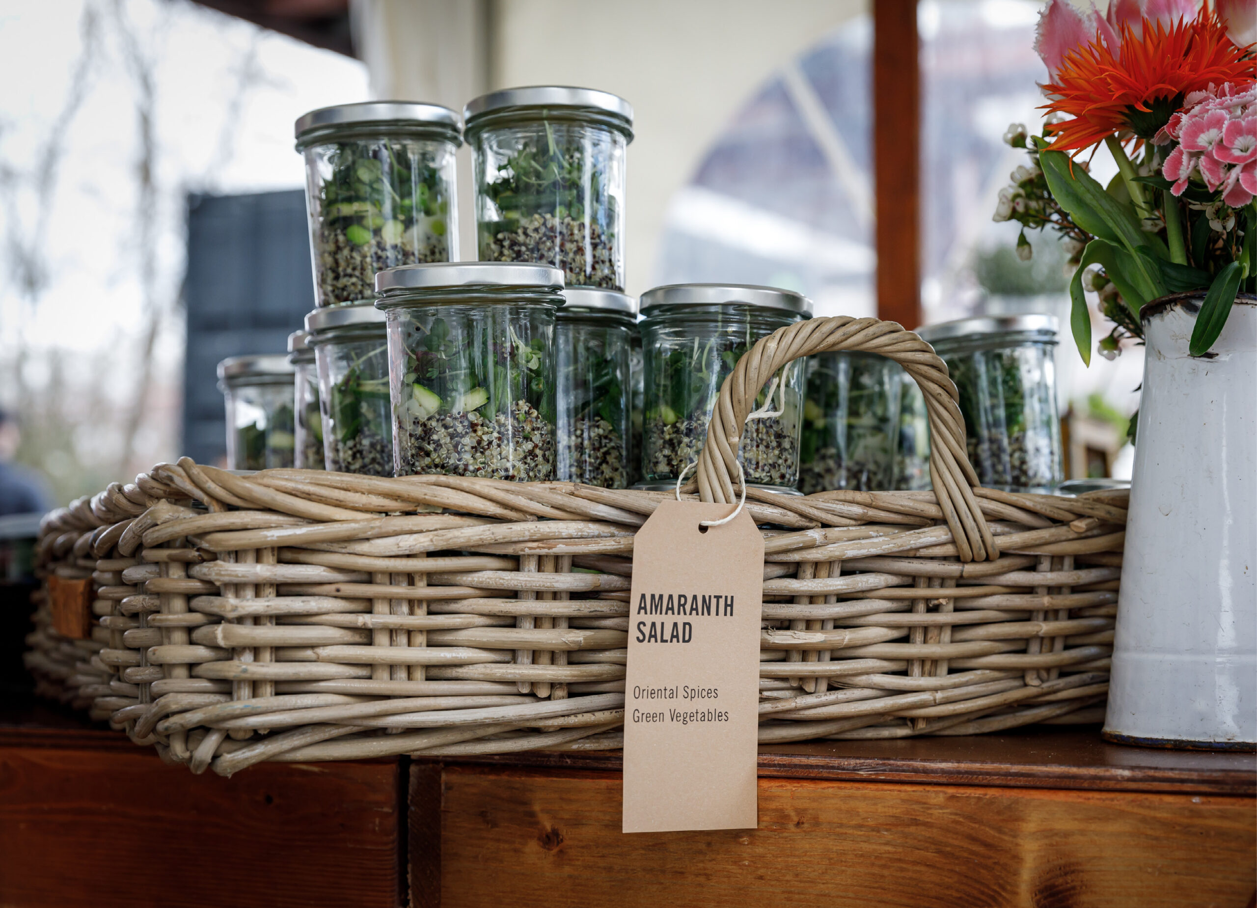 Gläser mit Amaranthsalat in einem Weidenkorb mit Etikett, daneben eine Vase mit Orangenblüten - perfekt für Catering für Tagungen und Konferenzen.