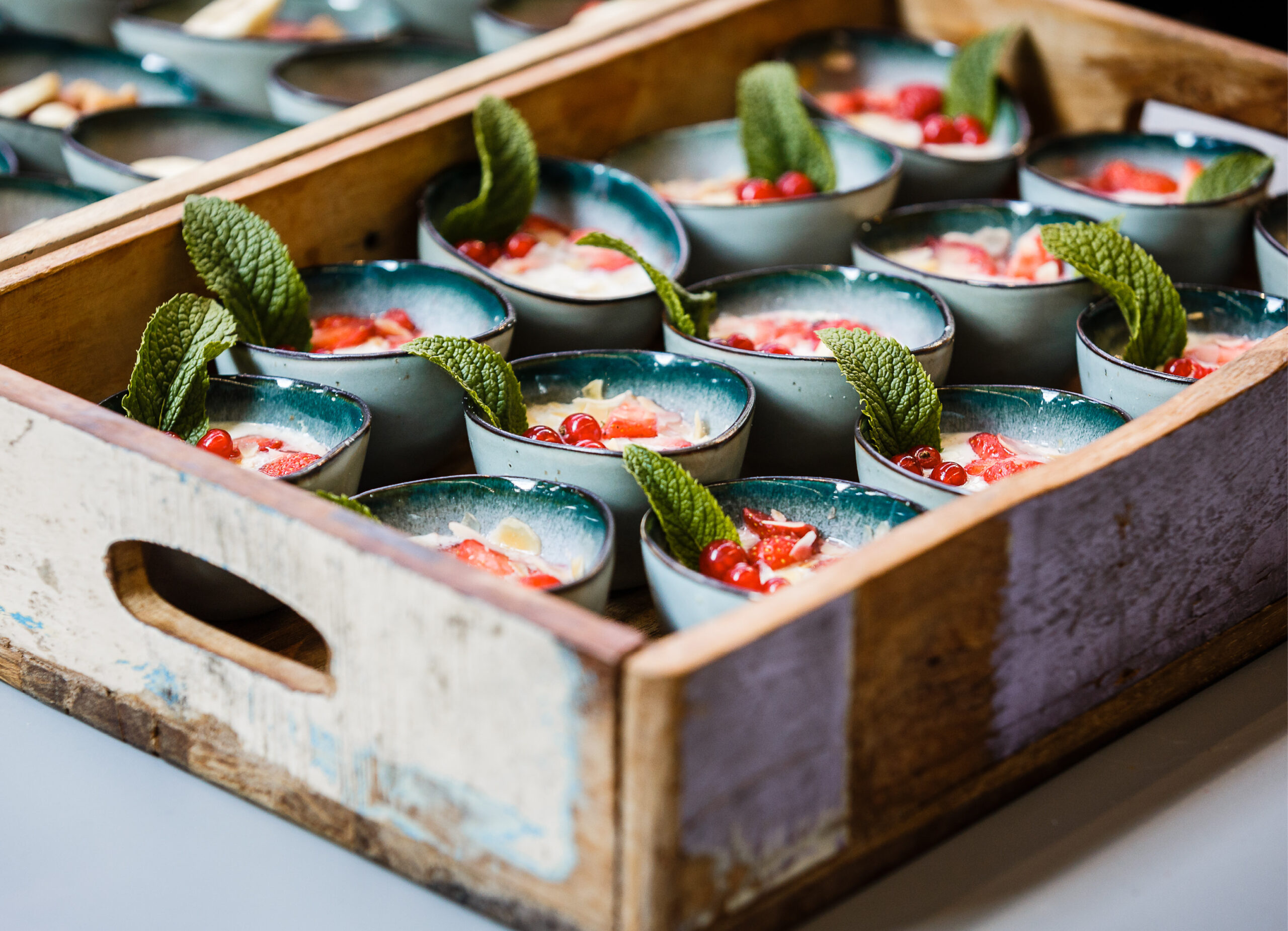 Auf einem Holztablett stehen kleine Dessertschälchen, die mit Minzblättern und roten Granatapfelkernen bestückt sind - perfekt für das Catering für Tagungen und Konferenzen.