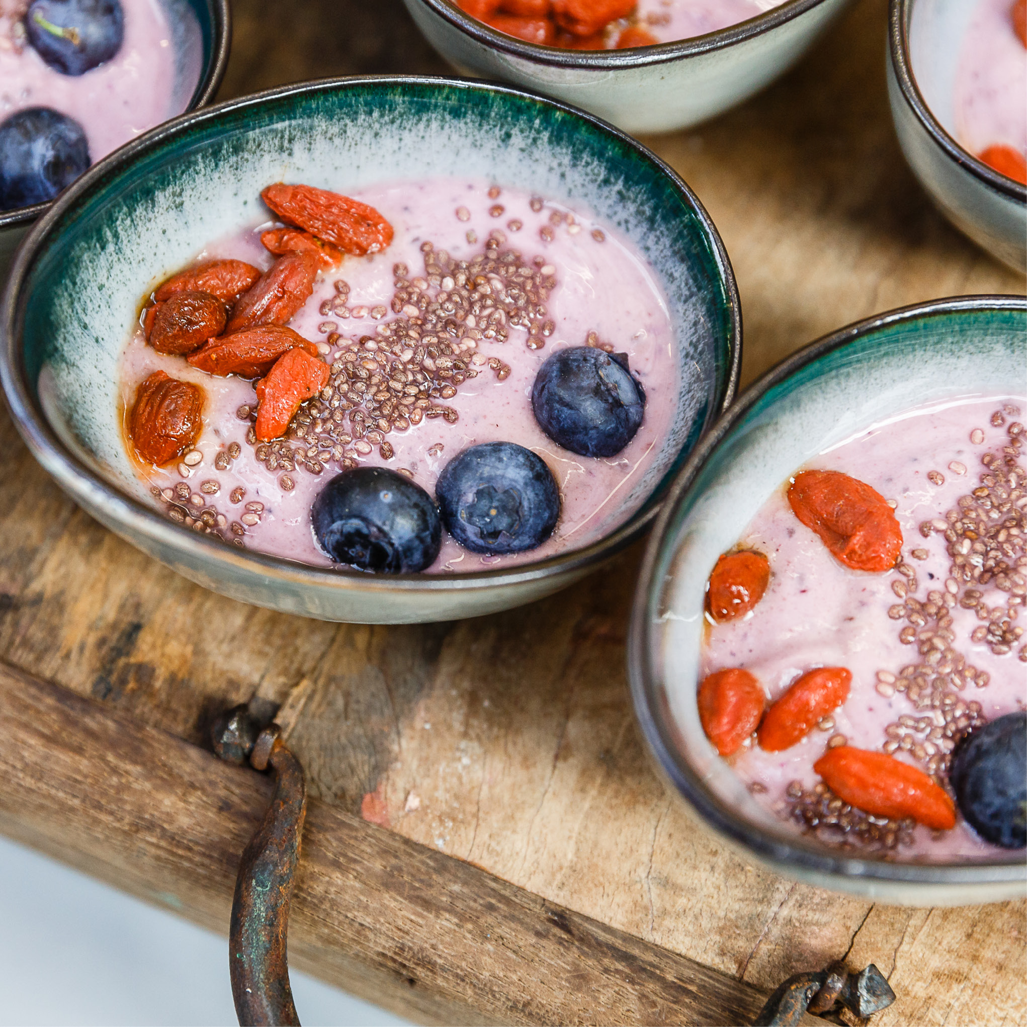 Schalen mit rosa Smoothie, perfekt für Catering für Tagungen und Konferenzen, mit Blaubeeren, Gojibeeren und Chiasamen auf einer rustikalen Holzoberfläche.