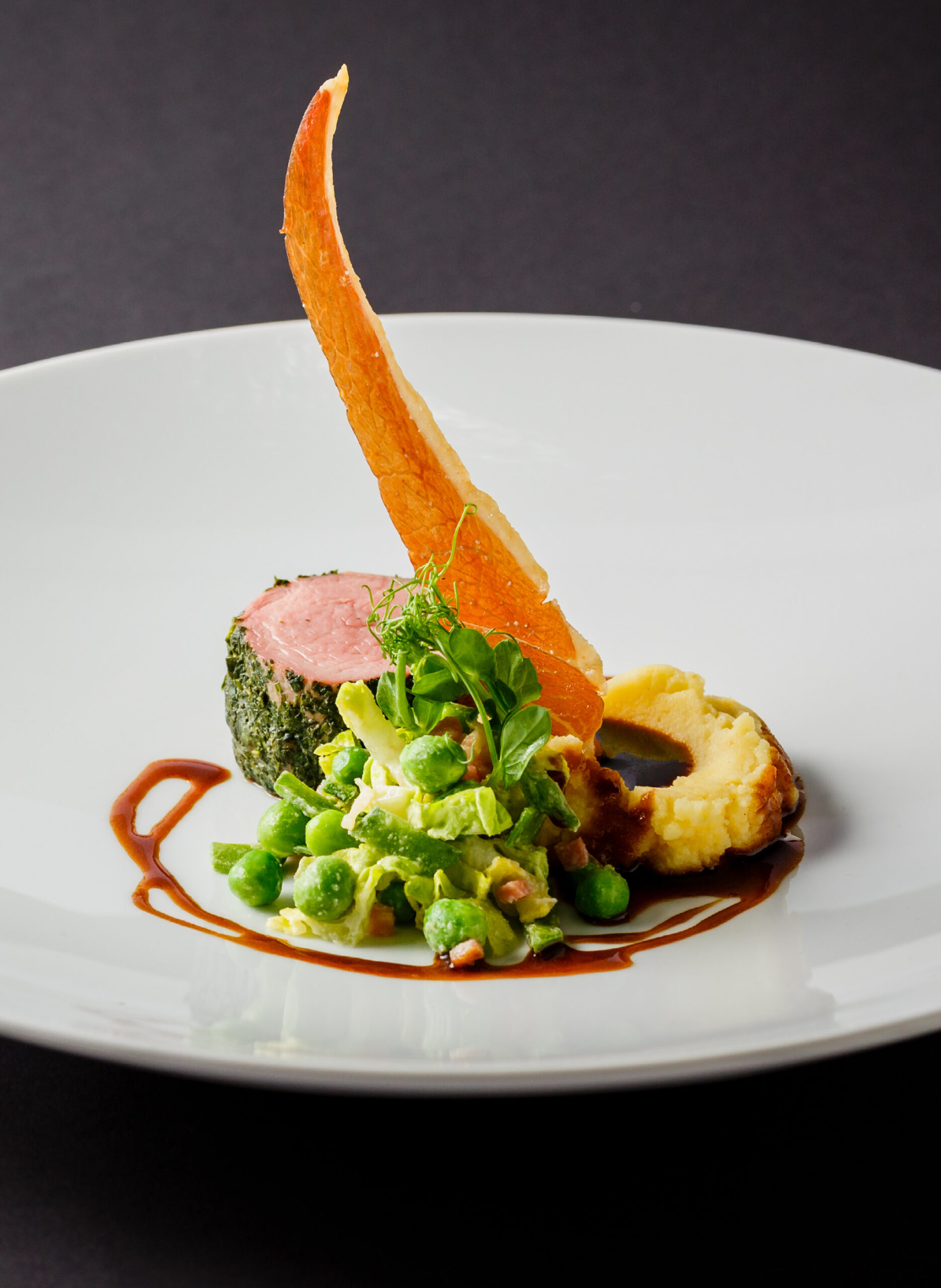 Gourmetteller mit Fleisch, grünem Gemüse, Sauce und einer knackigen Beilage auf einem weißen Teller.