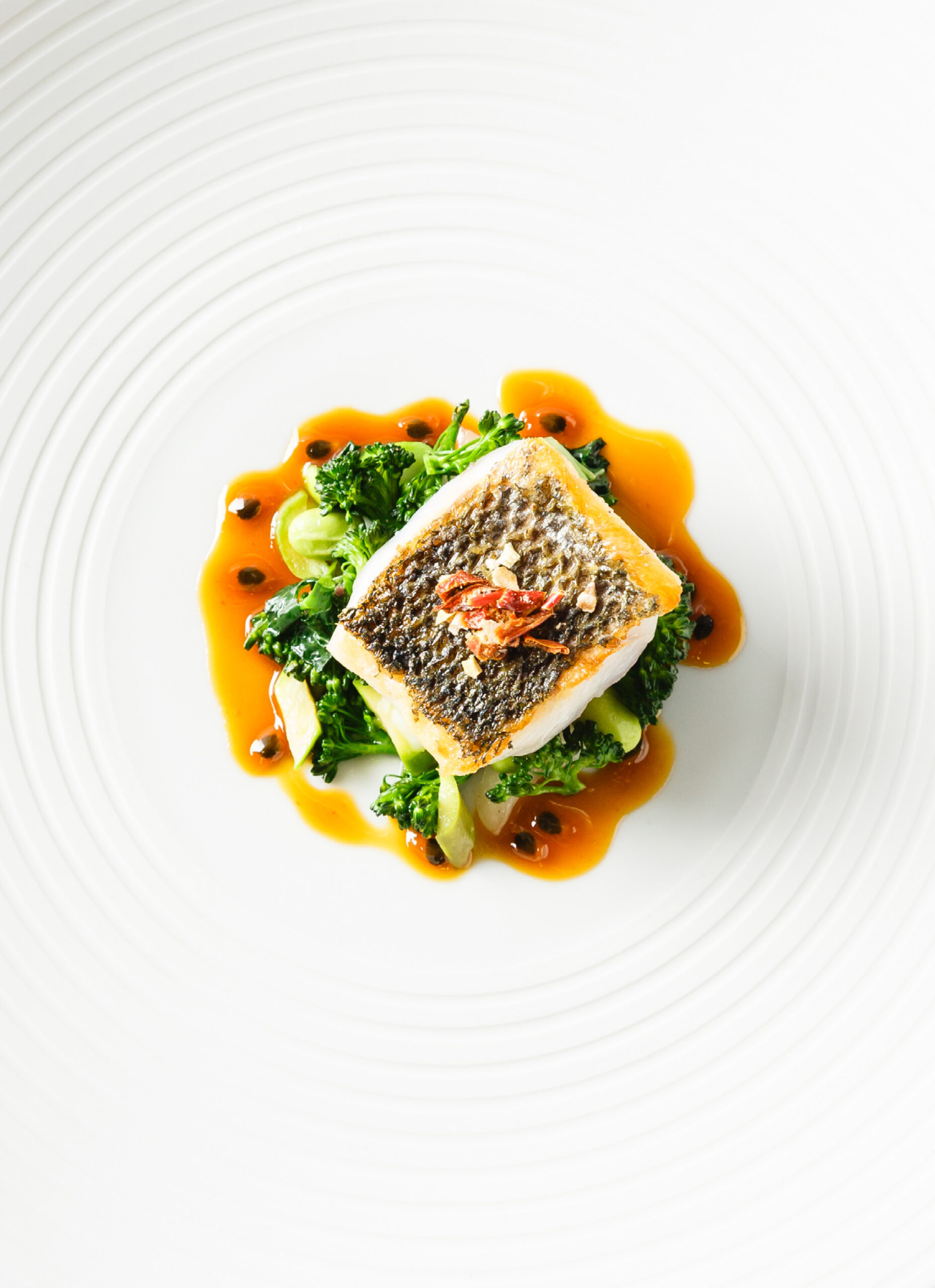 Ein Fischfilet auf sautiertem Gemüse mit Sauce, kunstvoll angerichtet auf einem weißen Teller mit strukturiertem Rand - perfekt für Catering für Tagungen und Konferenzen.