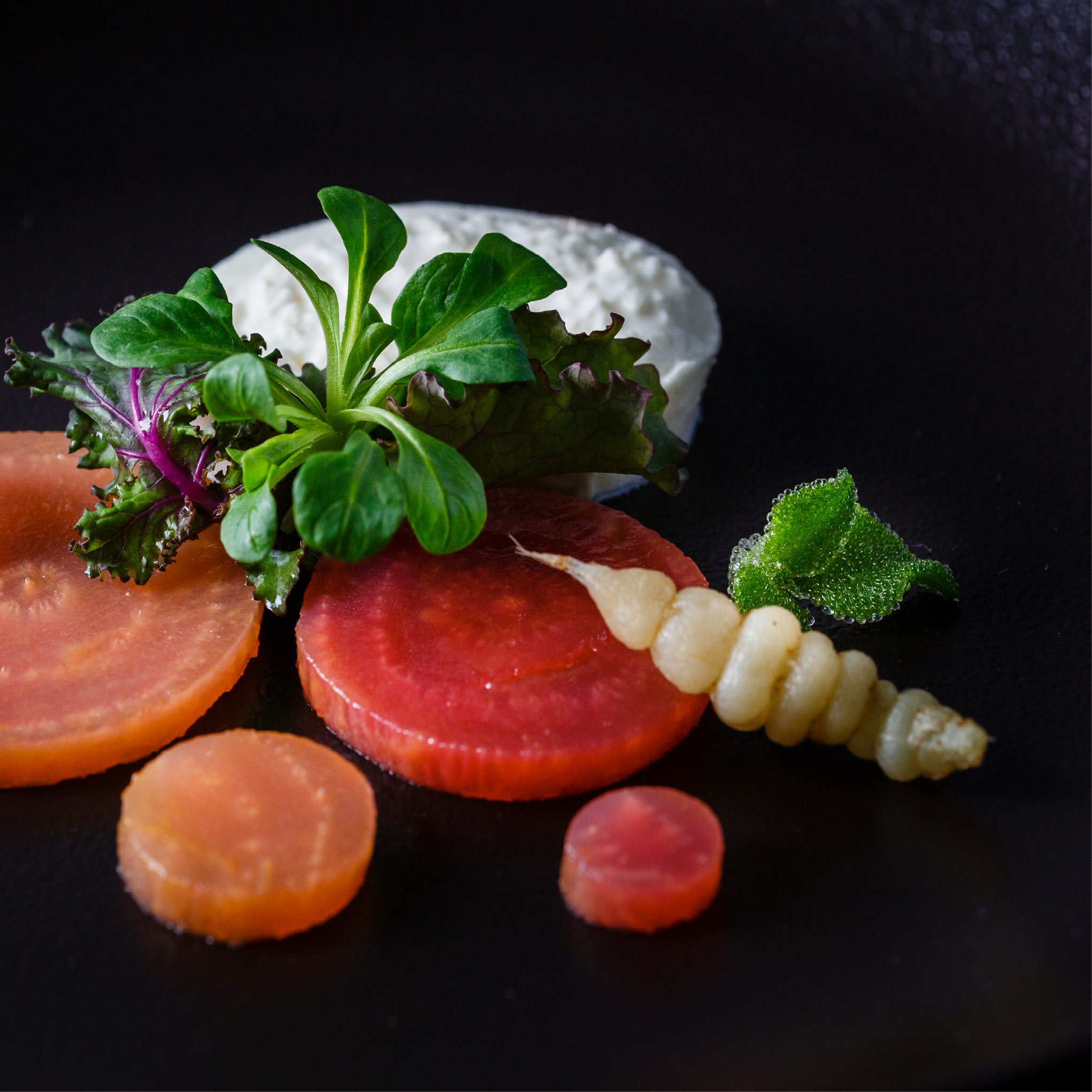 Gourmet-Salat mit buntem Wurzelgemüse, Grünzeug, weißer Sahne und einer essbaren Wurzelspirale auf einem schwarzen Teller - perfekt für Catering für Tagungen und Konferenzen.