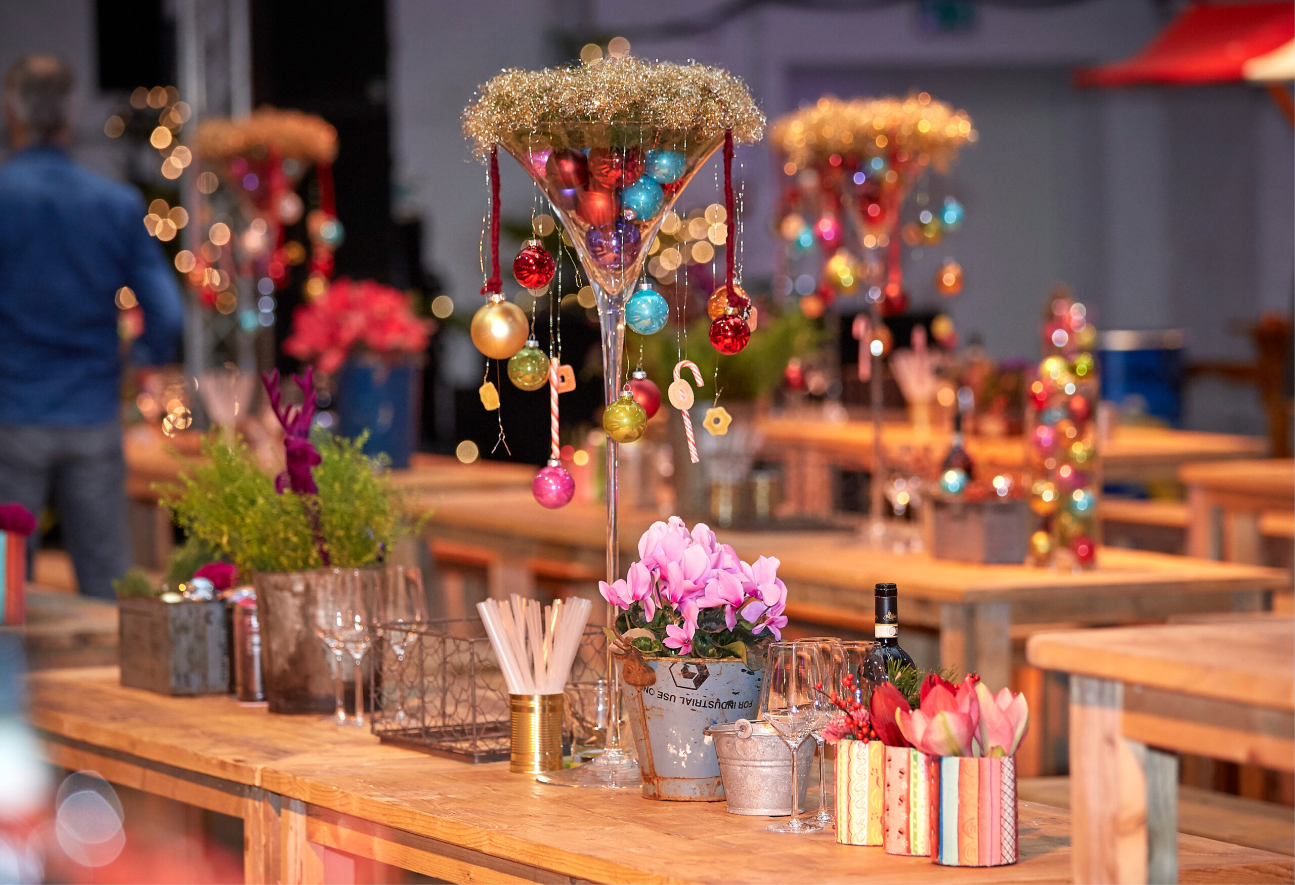 Große, mit Ornamenten und Lametta verzierte Cocktailgläser auf Holztischen, perfekt für festliche Innenräume oder Weihnachtsfeiern Catering in Köln.