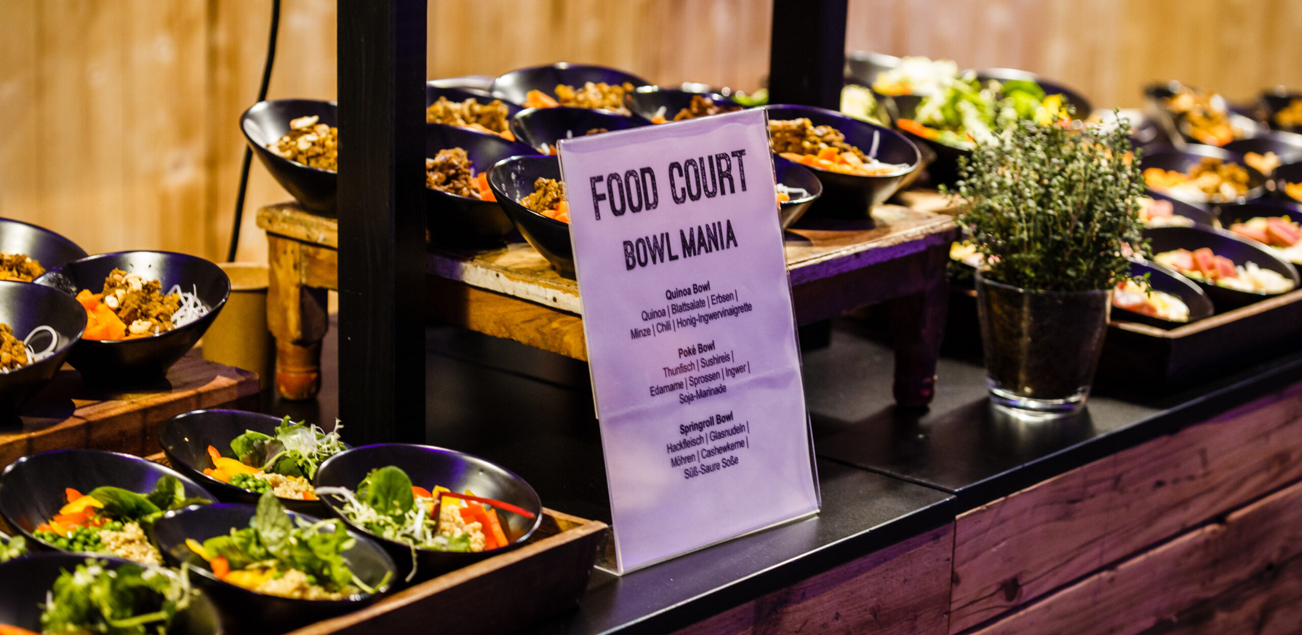 Ein Buffettisch mit verschiedenen bunten Salatschüsseln und einem Schild mit der Aufschrift "Food Court Bowl Mania" - ein ideales Setting für das Weihnachtsfeiern Catering in Köln.