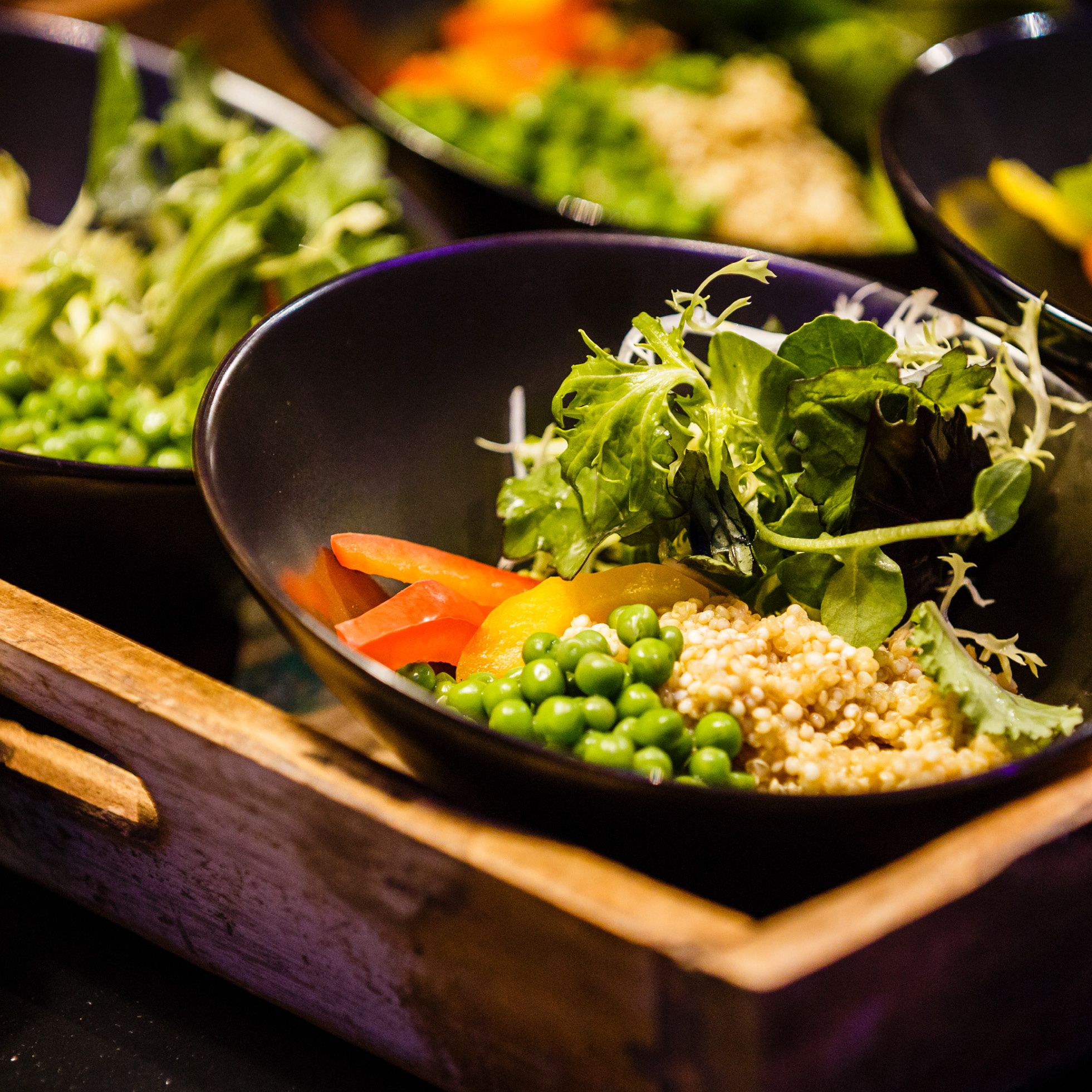 Eine Schüssel Quinoa-Salat mit grünen Erbsen, Blattgemüse und geschnittener Paprika auf einem Holztablett - perfekt für das festliche Weihnachtsfeiern Catering in Köln.