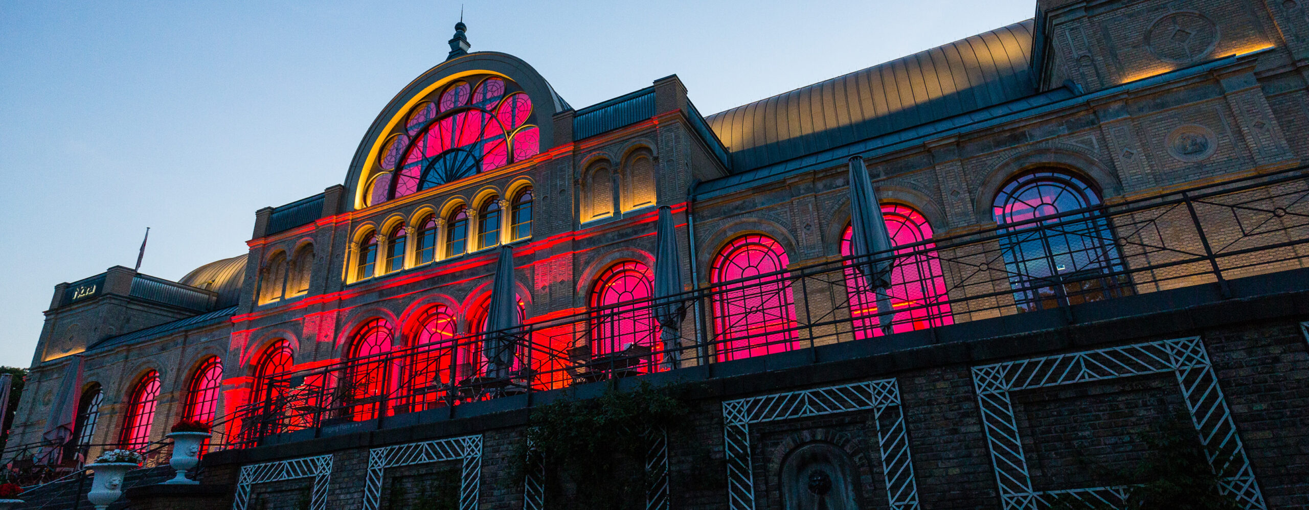 Ein großes historisches Gebäude mit Bogenfenstern, die in der Abenddämmerung in leuchtendem Rot und Rosa erstrahlen.