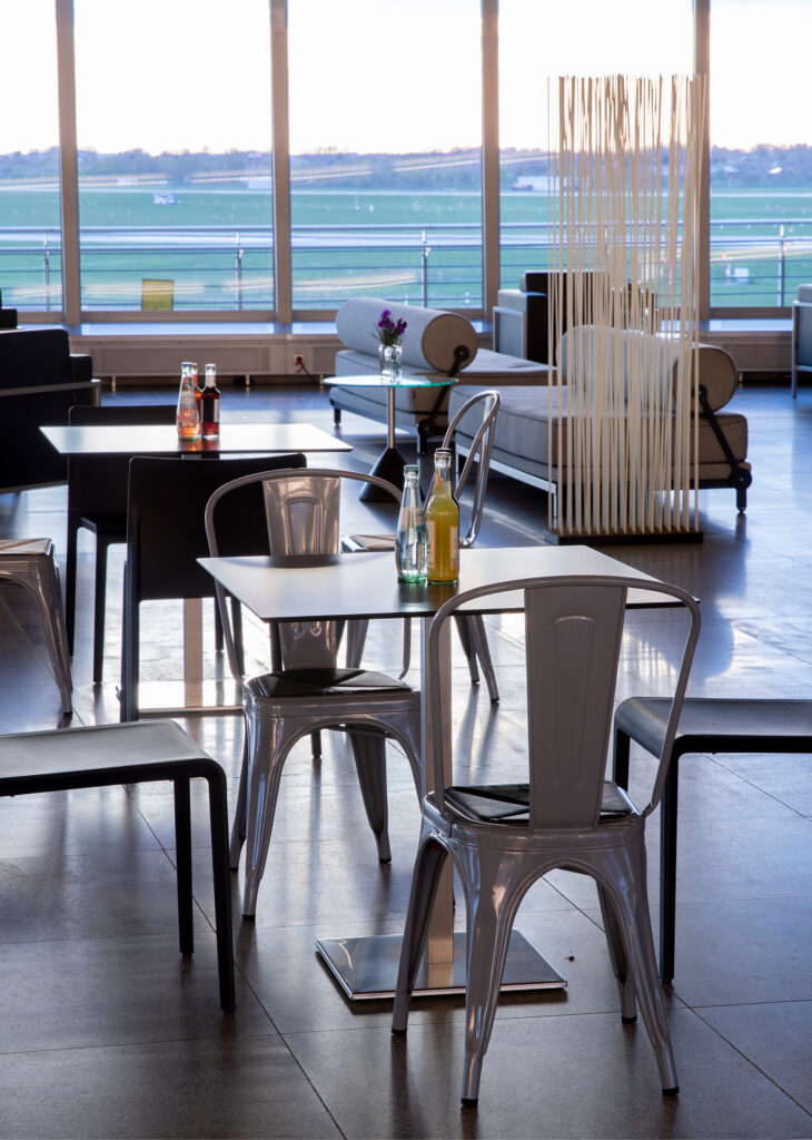 Moderne Flughafen-Lounge mit Metallstühlen, Tischen und Flaschengetränken, mit Blick auf die Landebahn durch große Fenster - ideal für alle, die Eventlocations Köln mieten und eine einzigartige Atmosphäre suchen.