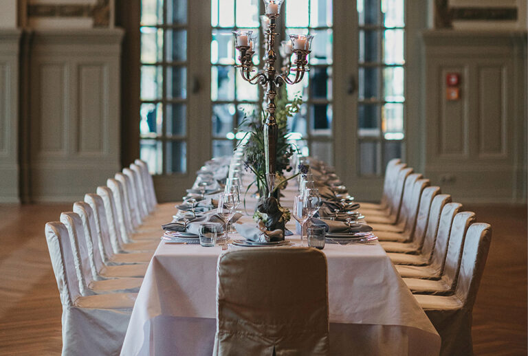 Eleganter langer Esstisch für eine formelle Veranstaltung mit weißer Tischwäsche, Kerzen und ordentlich angeordneten Stühlen – perfekt für Catering in Bad Honnef.