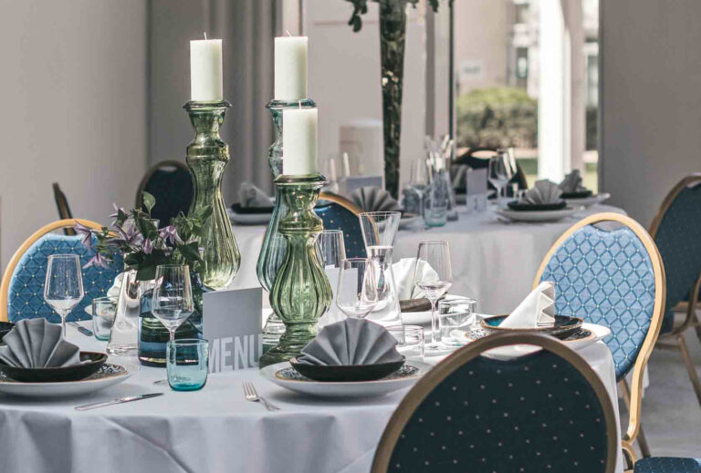 Elegante Tischdekoration mit gefalteten Servietten, Gläsern, grünen Kerzenleuchtern und einem Blumengesteck – perfekt für das Catering in Bad Honnef.