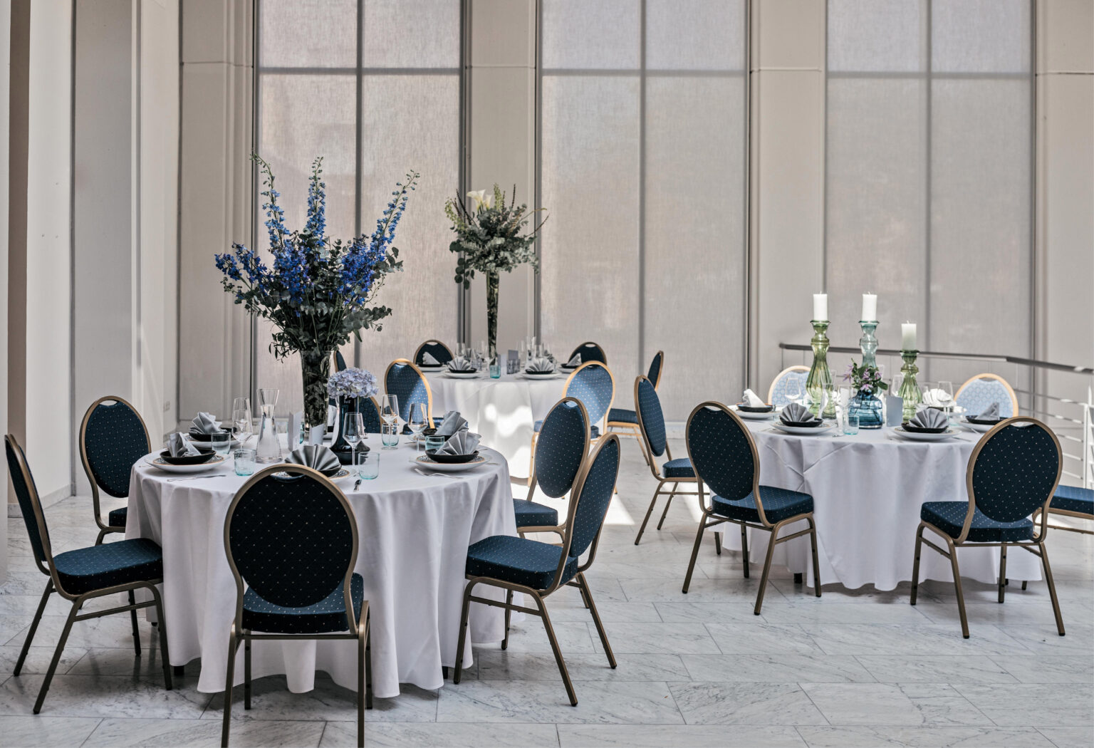 Elegante Banketttische mit blauen Stühlen, weißen Tischdecken und floralen Tischdekorationen in einem sonnendurchfluteten Raum – perfekt für Catering in Bad Honnef.
