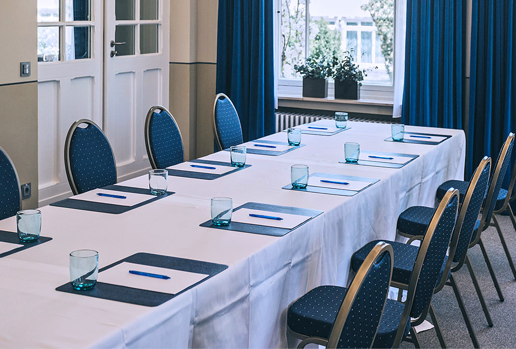 Ein Konferenztisch-Set mit Notizblöcken, Stiften, Gläsern und blauen Stühlen – ideal für Meetings oder Events mit Catering in Bad Honnef.