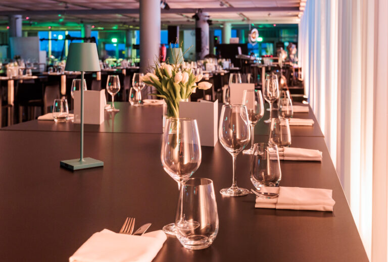 Eleganter Restauranttisch mit Glasgeschirr, gefalteten Servietten und einer Vase mit weißen Blumen unter sanfter Beleuchtung.