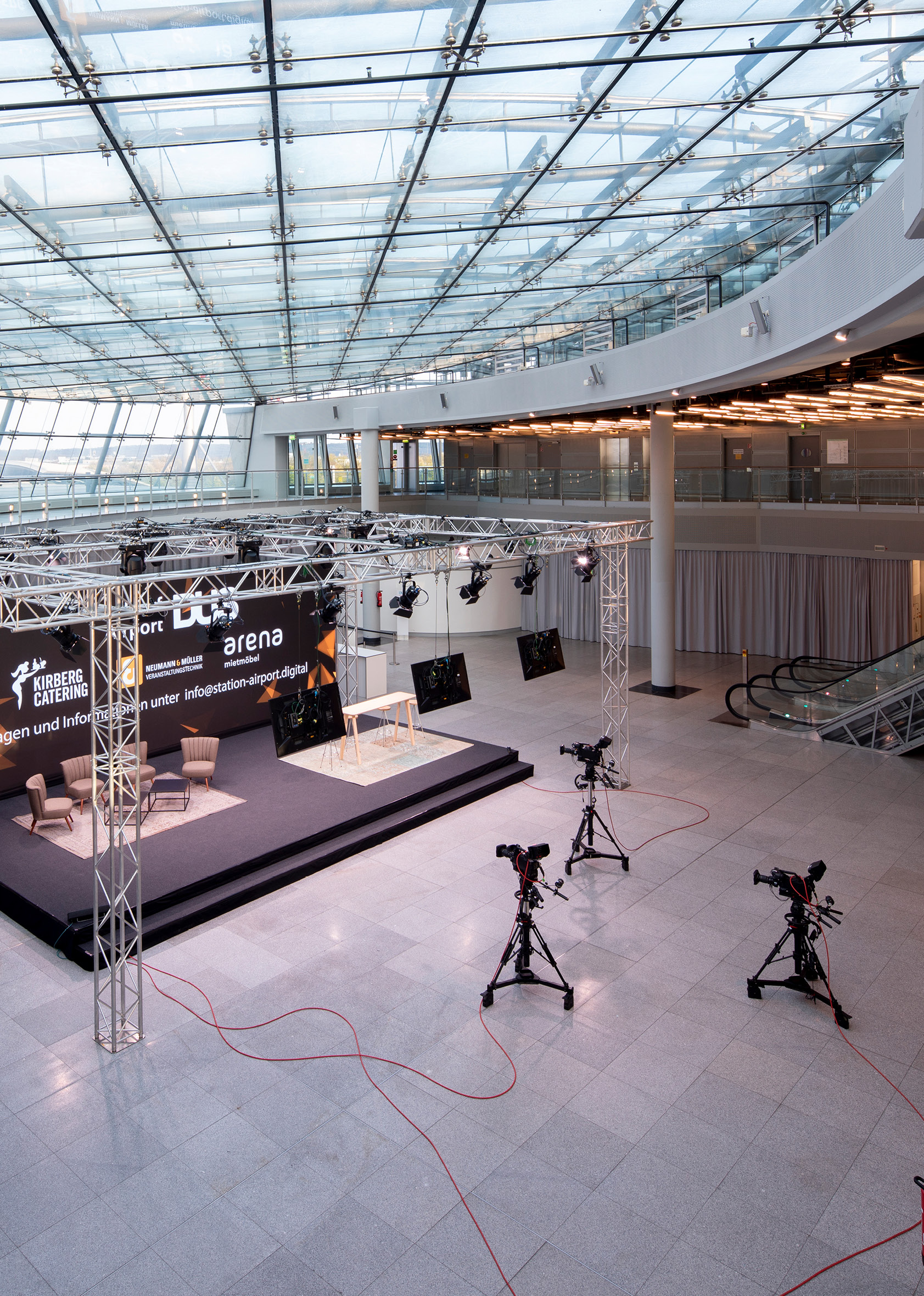 Moderner Indoor-Veranstaltungsraum mit Bühne, Kameras und Glasdach in der Station Airport für Veranstaltungen, eingerichtet für eine Live-Übertragung oder Präsentation.