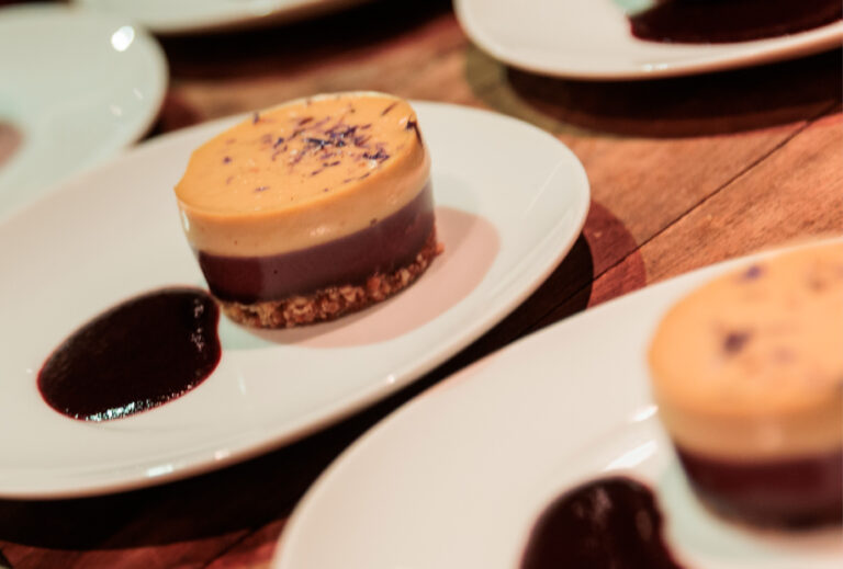 Ein angerichtetes Dessert mit geschichteter Mousse und Soße auf einem weißen Teller, angerichtet auf einem Holztisch im Station Airport für Veranstaltungen.