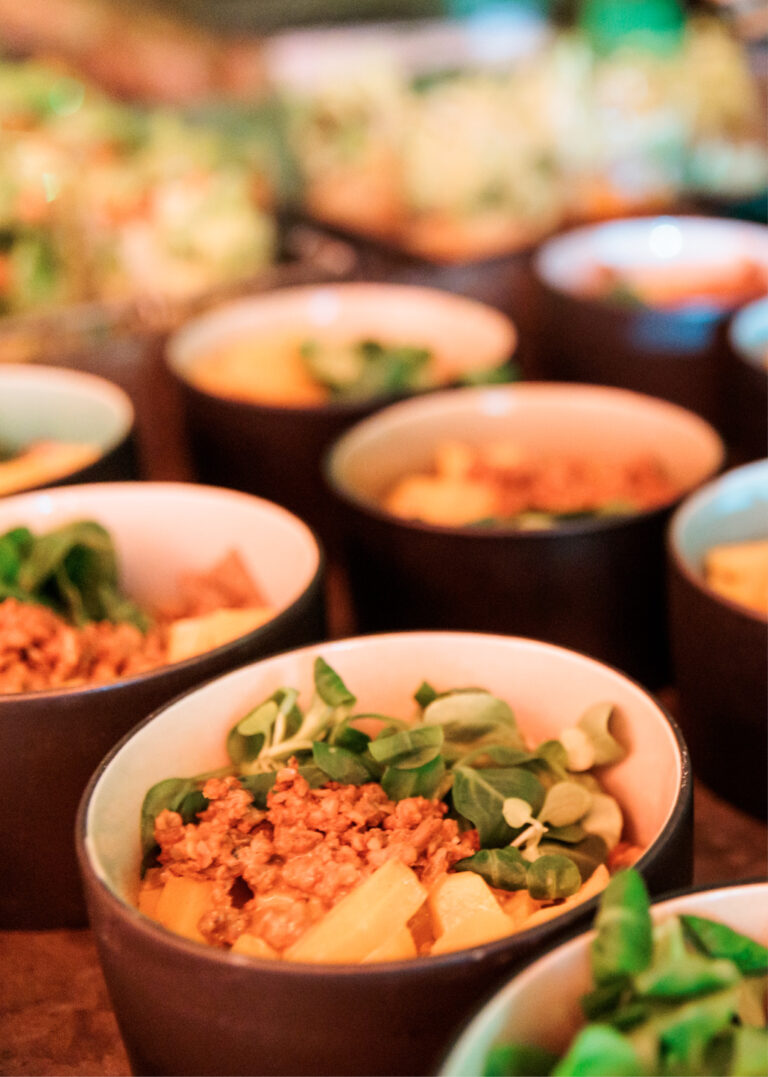 Dicht an dicht stehen mehrere Schalen gefüllt mit Gemüse, Granola und gelben Früchten auf einem Tisch in der Station Airport für Veranstaltungen.