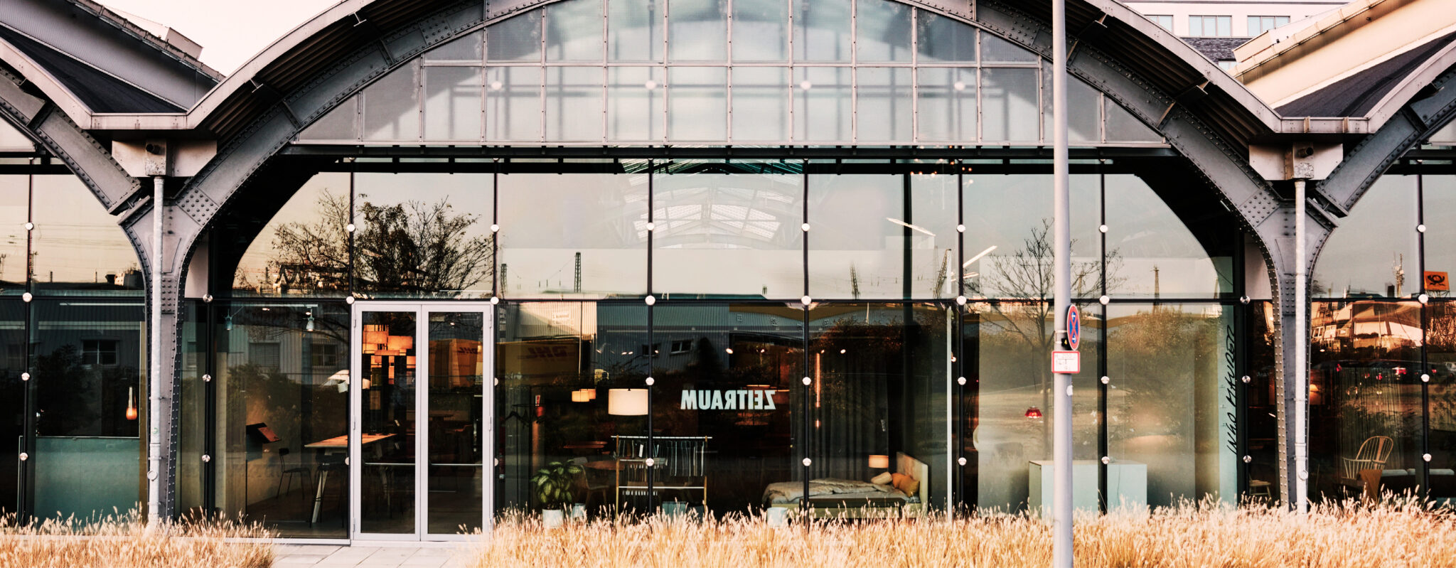 Moderner Glasbau mit gewölbtem Dach, leuchtenden Innenlichtern und hohem Gras davor – perfekt als Design Post als Eventlocation für unvergessliche Zusammenkünfte.