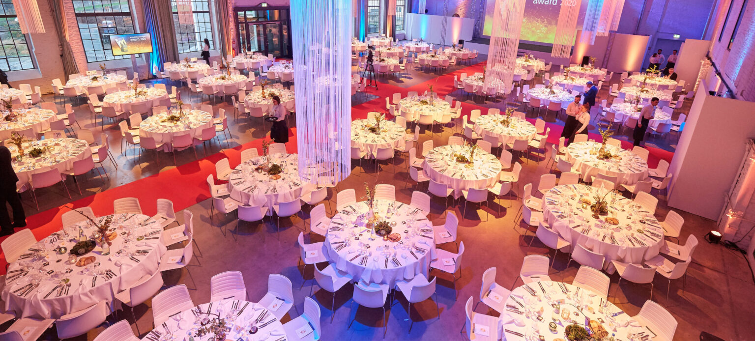 Eleganter Bankettsaal im Dock 2 in Köln für Events mit runden, festlich gedeckten Tischen, wunderschön mit Blumen dekoriert und in warmes Licht getaucht.